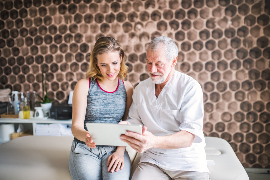 Senior male physiotherapist and young woman with tablet sitting. by Jozef Polc on 500px.com