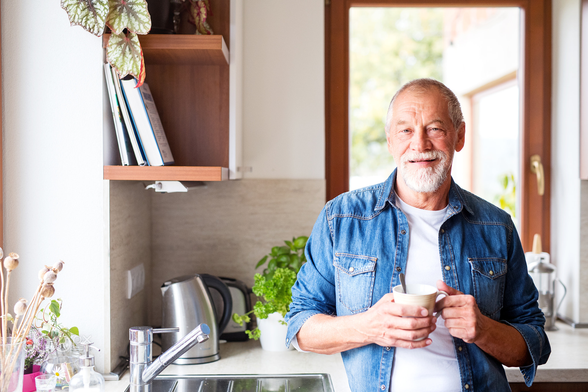 Senior man holding a cup of coffee in the kitchen.