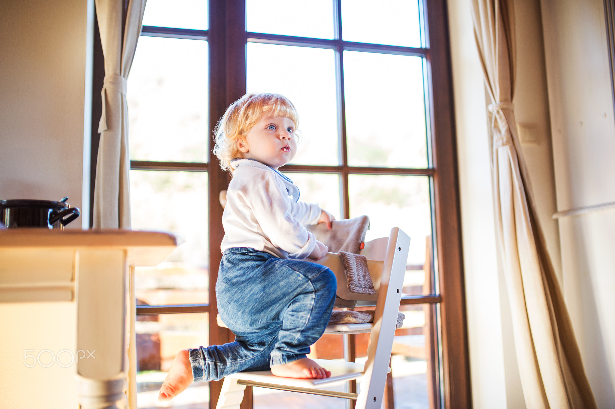 Toddler boy in a dangerous at home, climbing into highchair.