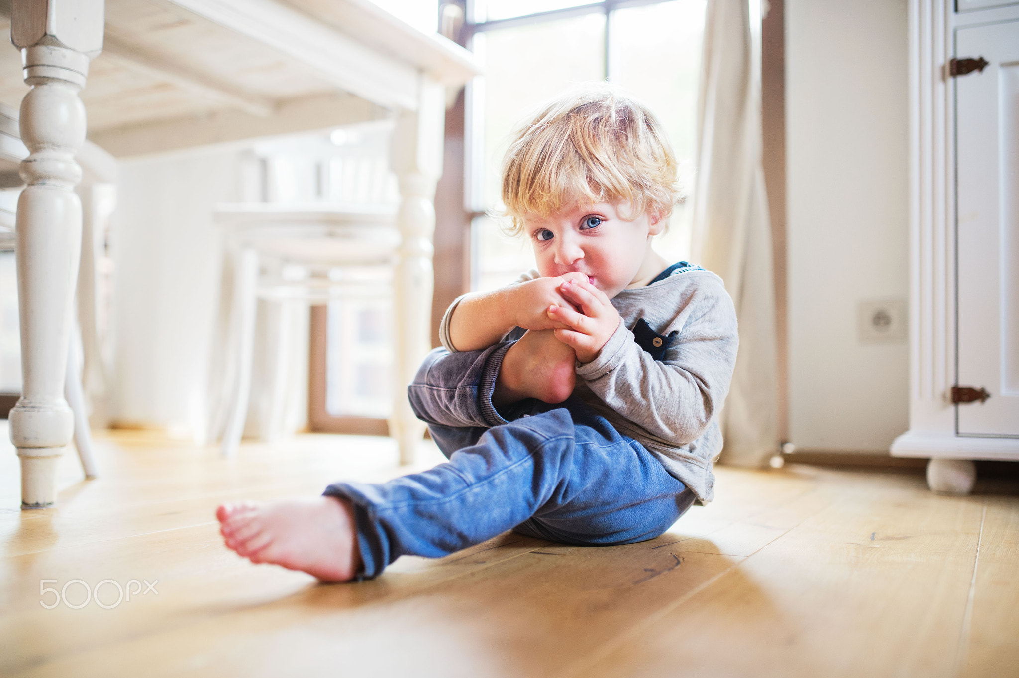 A toddler boy sitting on the floor at home.