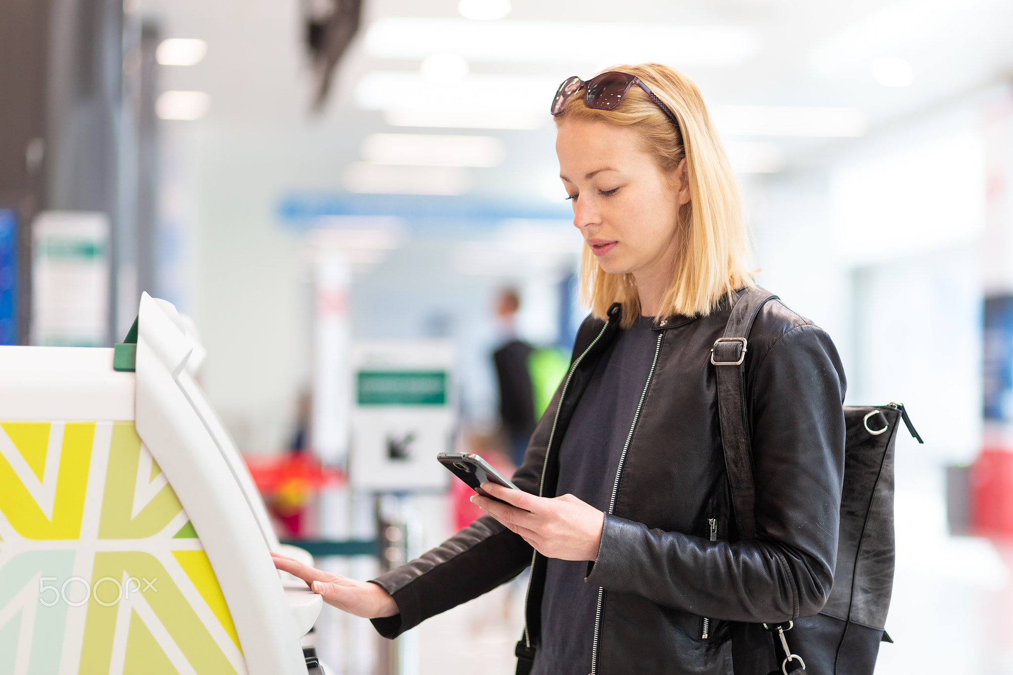 Casual caucasian woman using smart phone application and check-in machine at the airport getting...