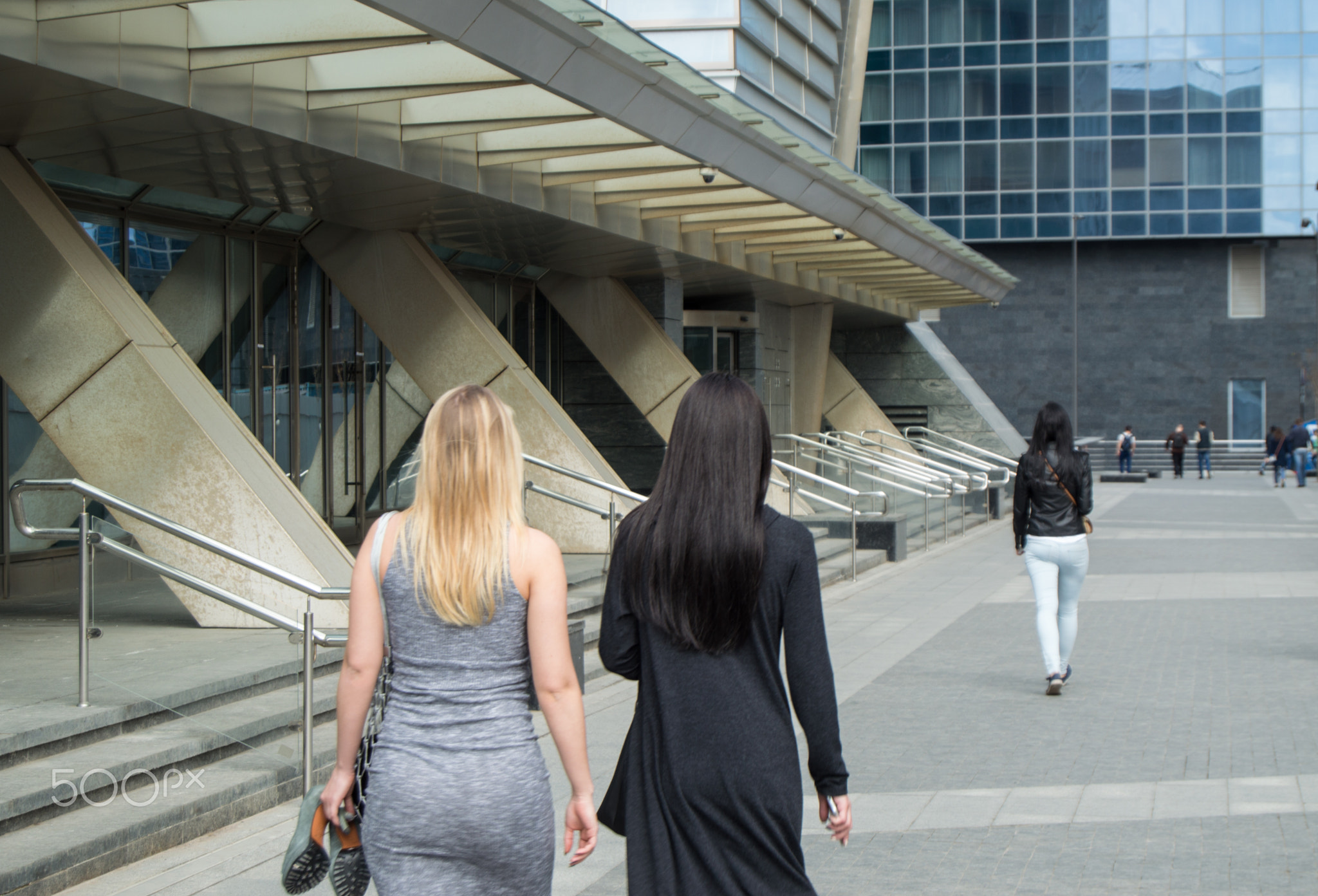 Two girls blonde and brunette with long hair walking on the street near the business center. The...