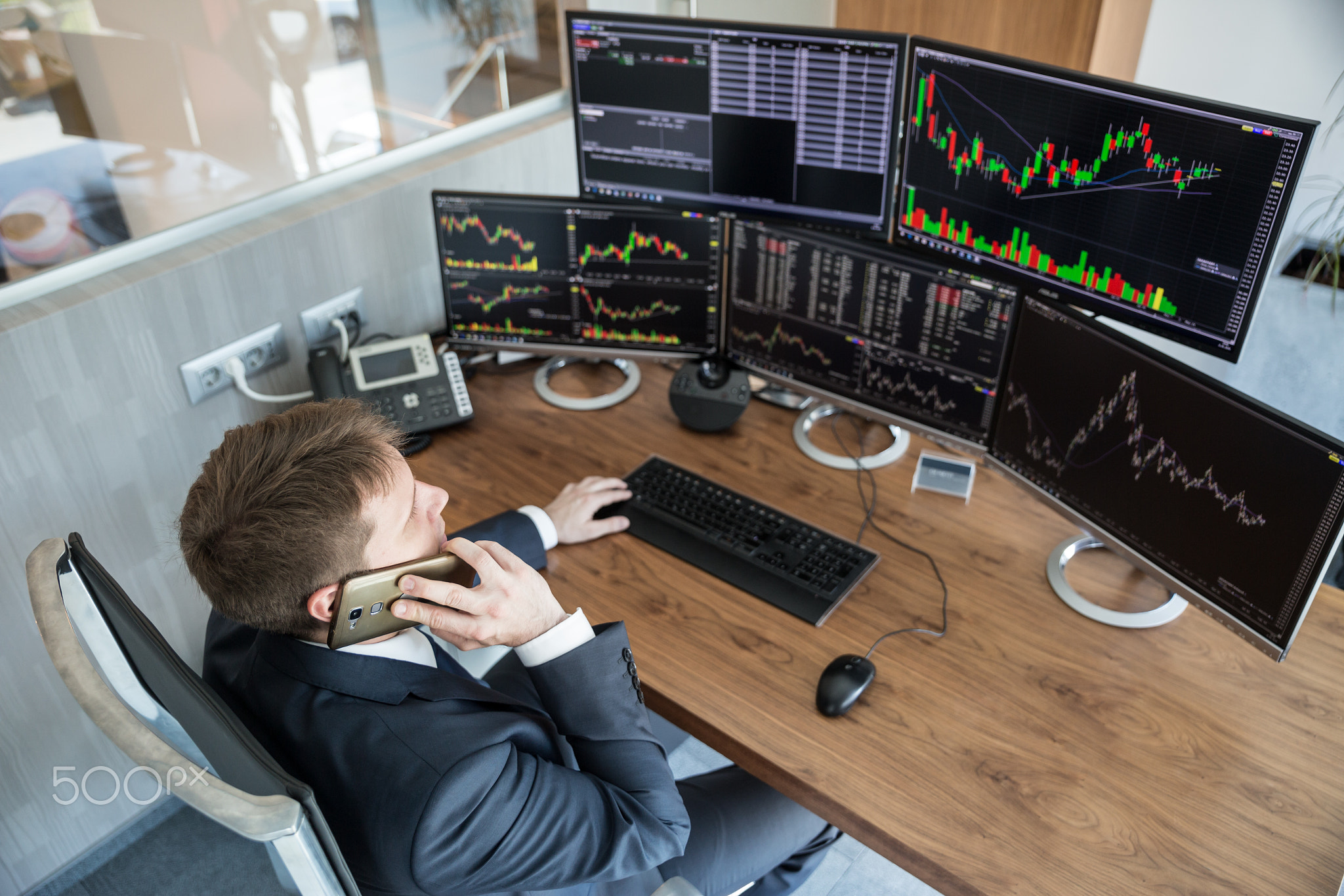 Over the shoulder view of stock broker trading online, talking on mobile phone.