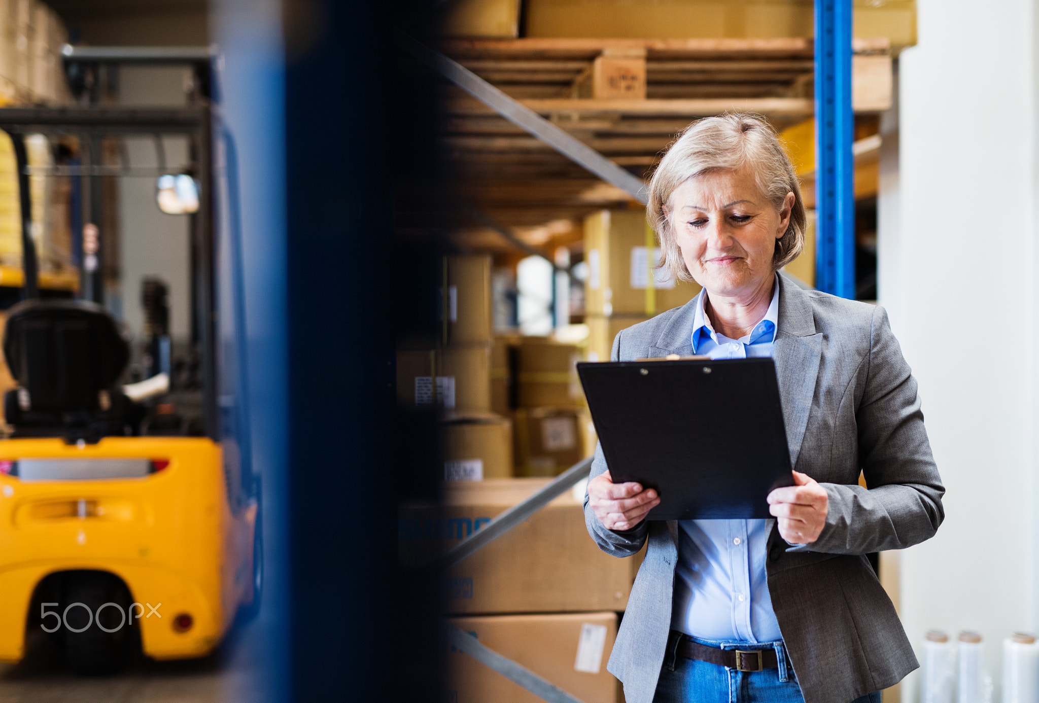 Senior woman warehouse manager or supervisor with clipboard.