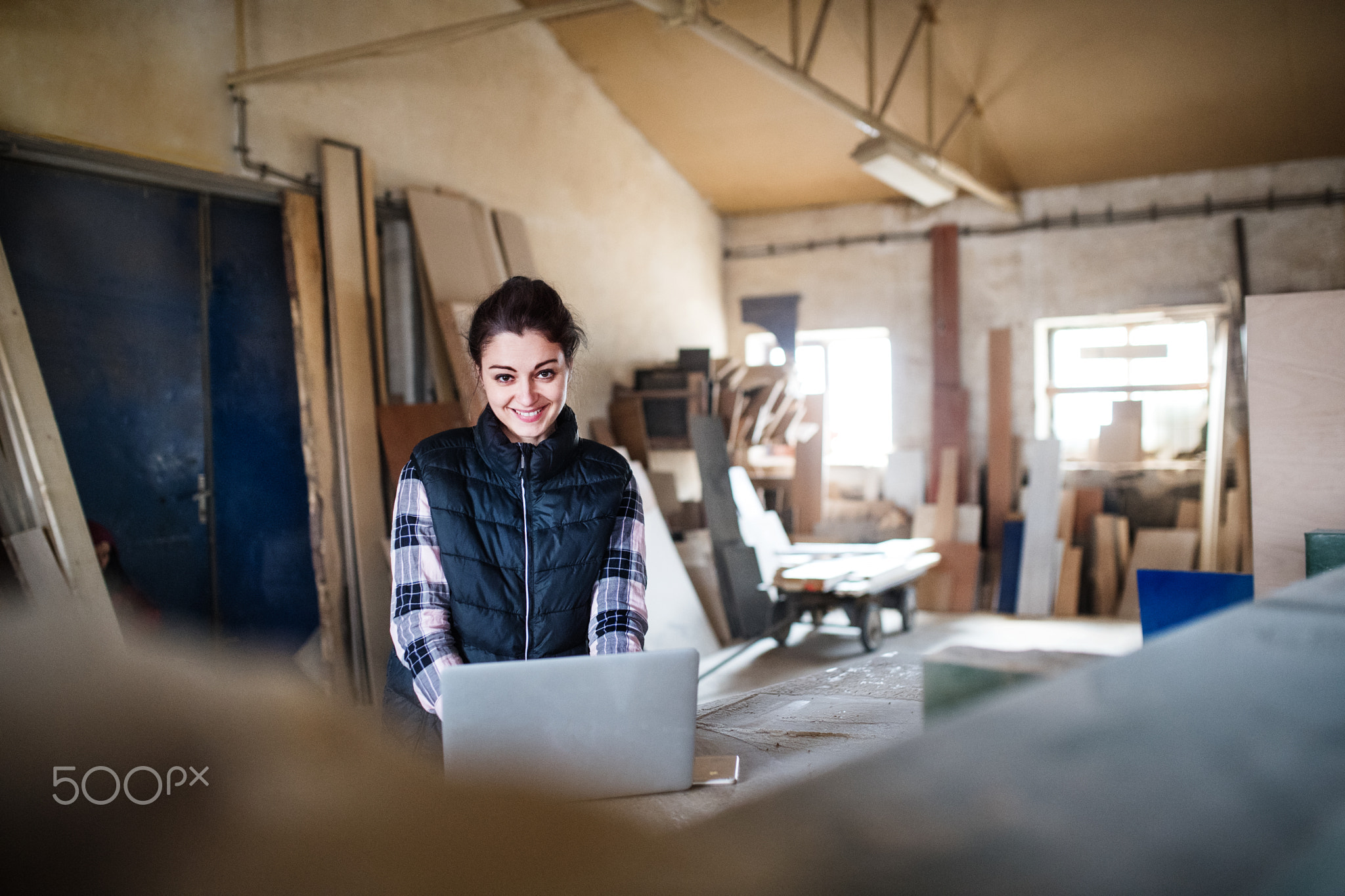 Portrait of a woman worker with laptop in the carpentry workshop.