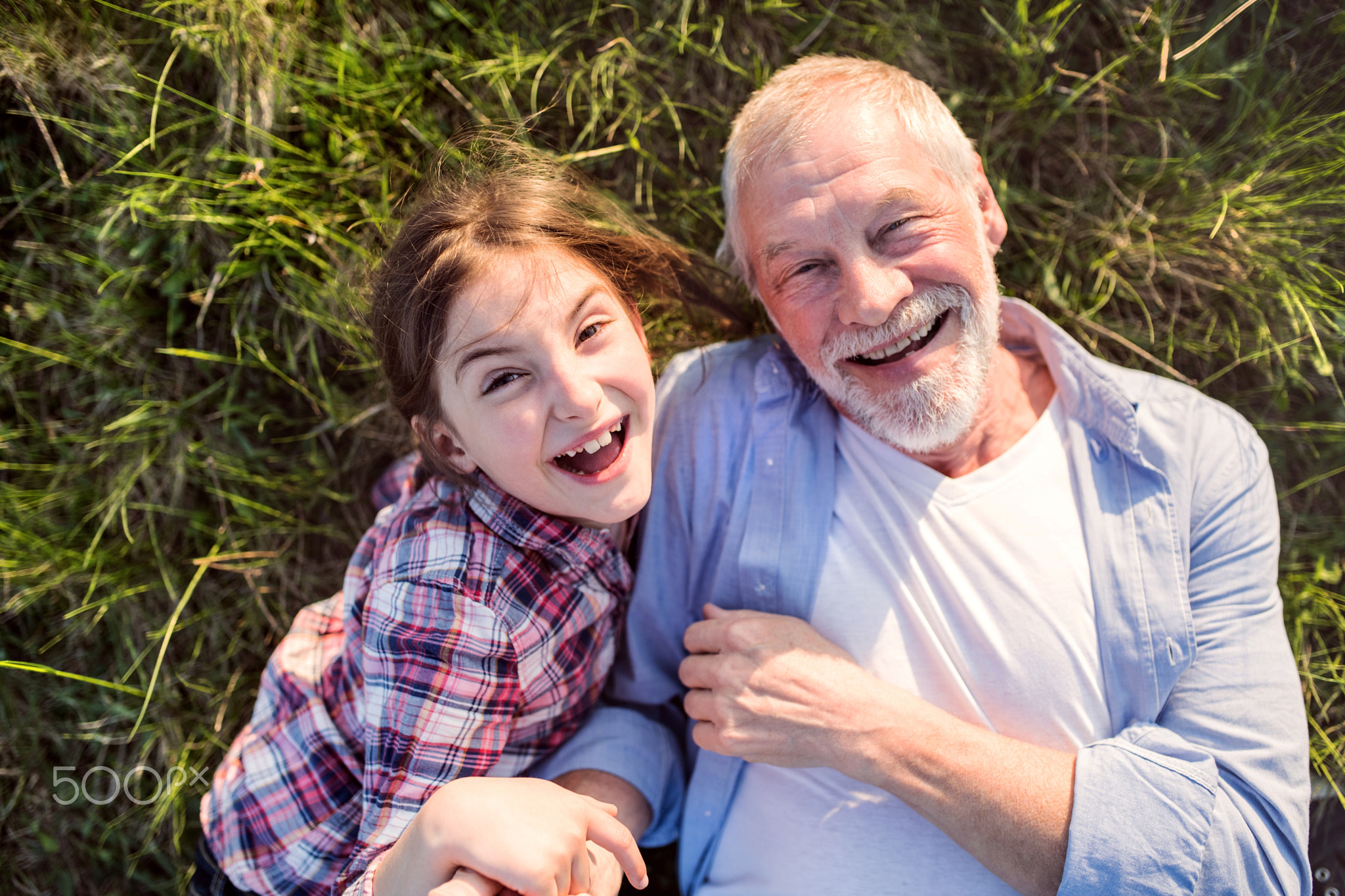 A small girl with grandfather outside in spring nature, relaxing on the grass.