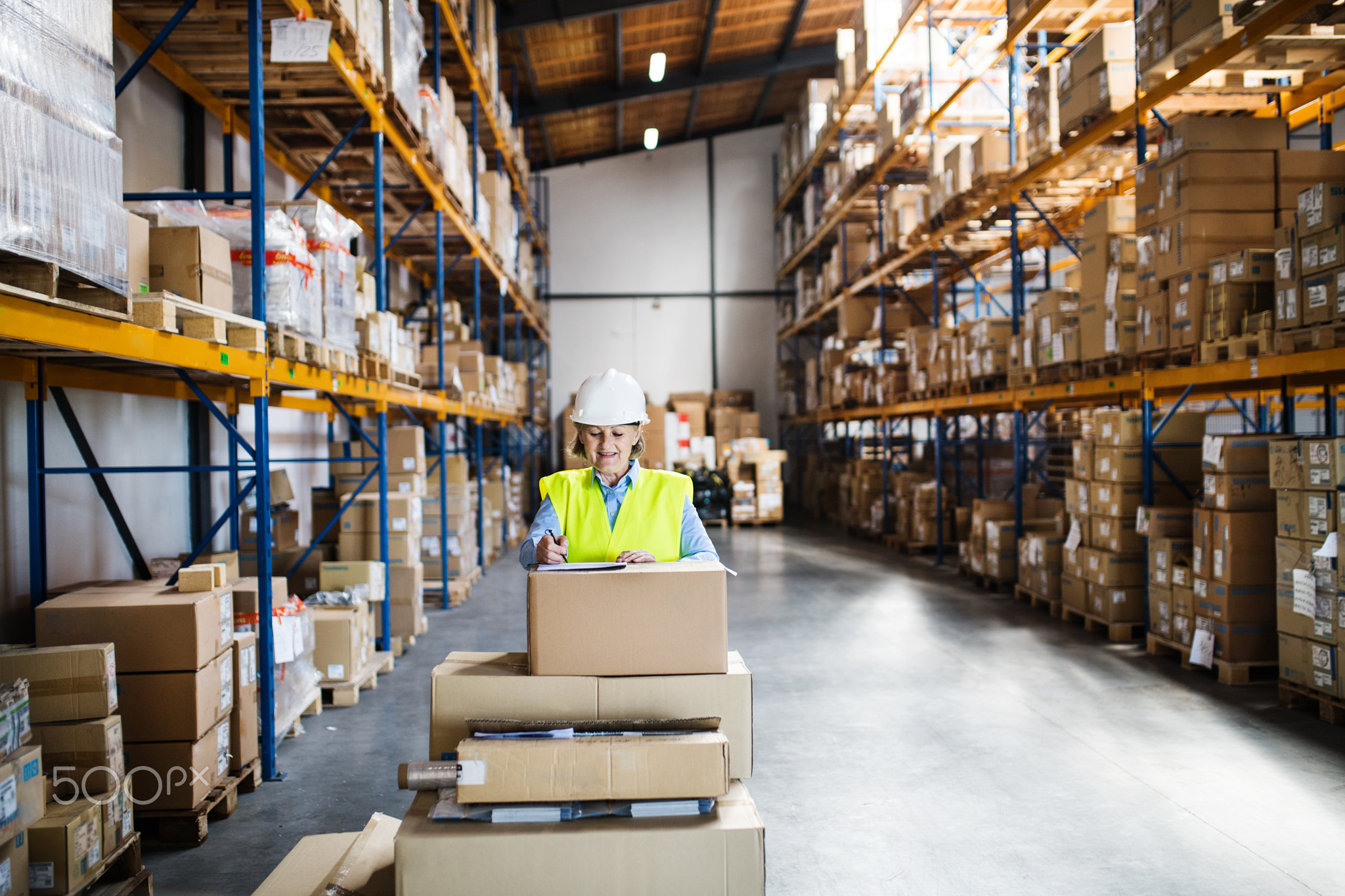 A senior woman warehouse worker or supervisor controlling boxes.