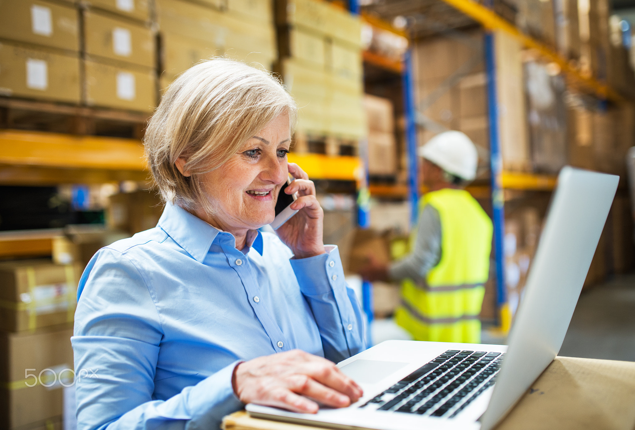 Senior woman manager with smartphone and man worker working in a warehouse.