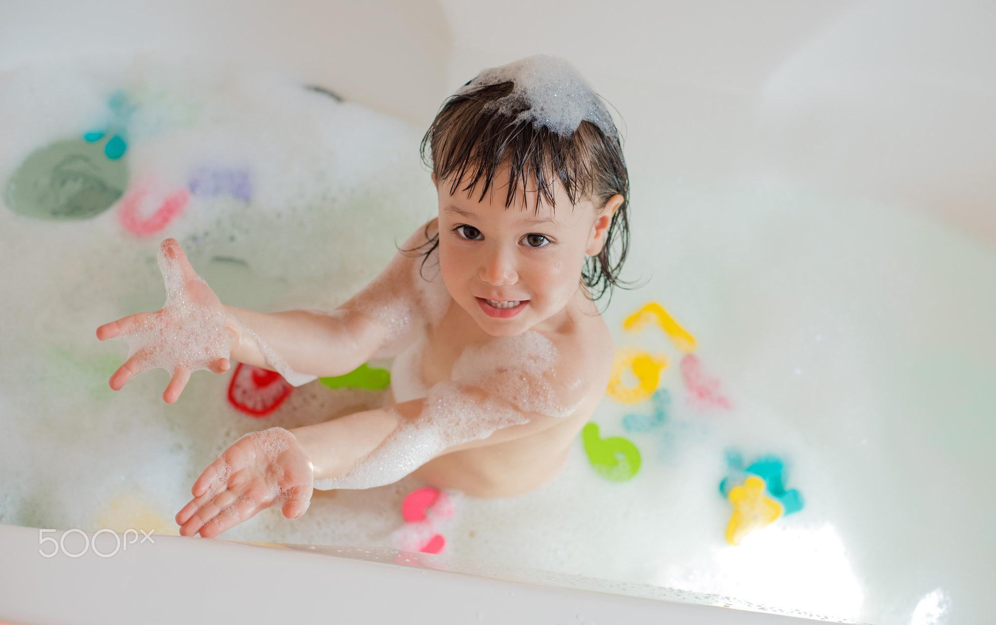 Happy little baby in the bathroom playing with foam bubbles and letters. Hygiene and care for...