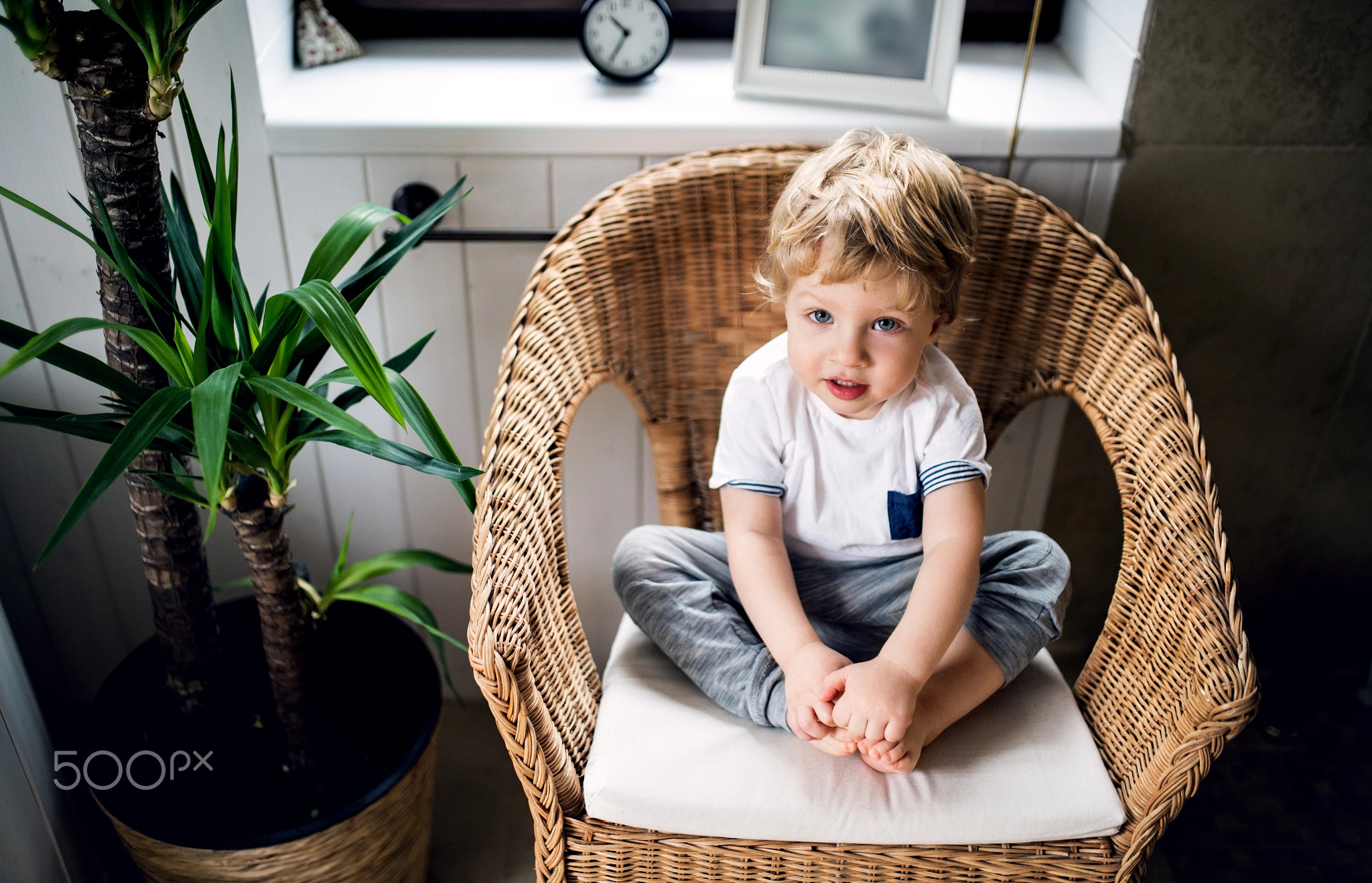 A toddler boy sitting on the wicker chair in the bathroom at home.