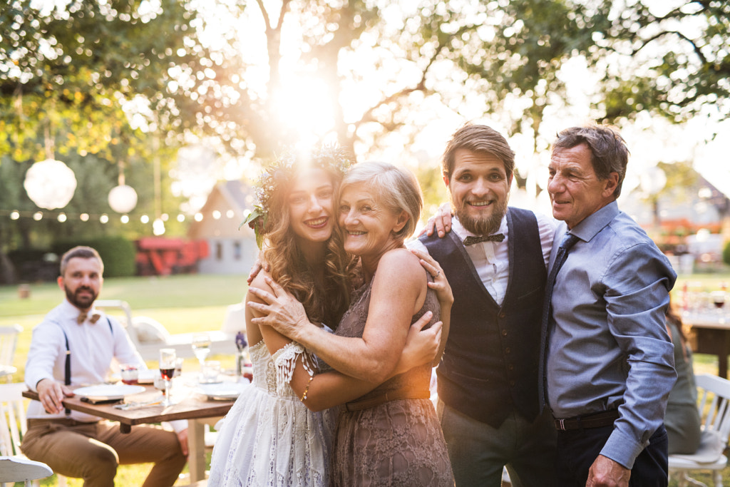 Bride, groom with parents posing for the photo at wedding reception outside in the backyard. by Jozef Polc on 500px.com