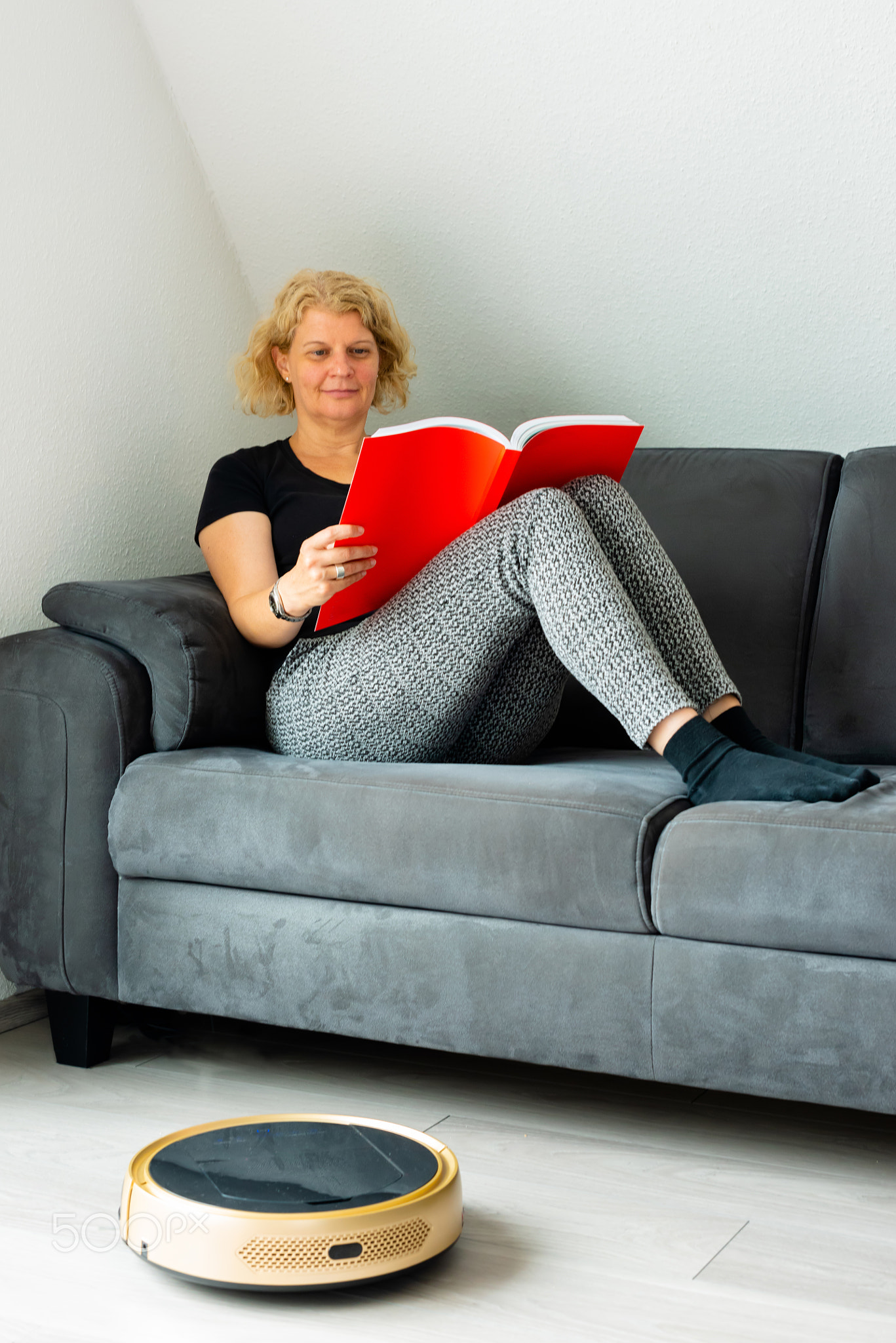 Vacuum cleaning robot with relaxed woman reading in the background