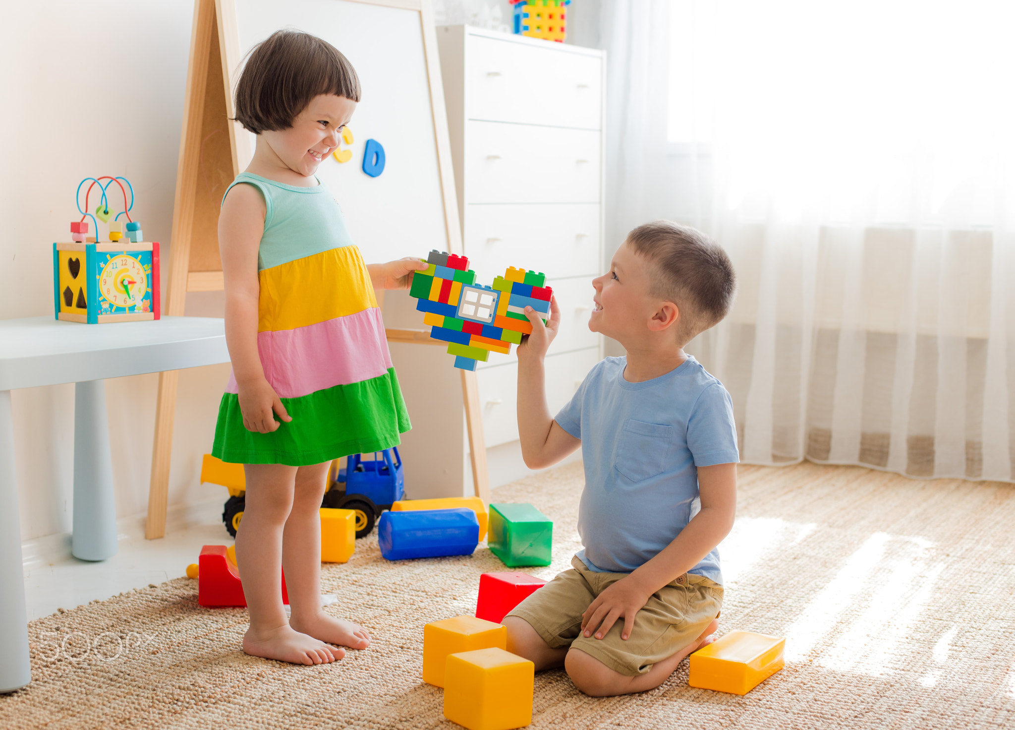 A boy and a girl are holding a heart made of plastic blocks. Brother and sister have fun playing...