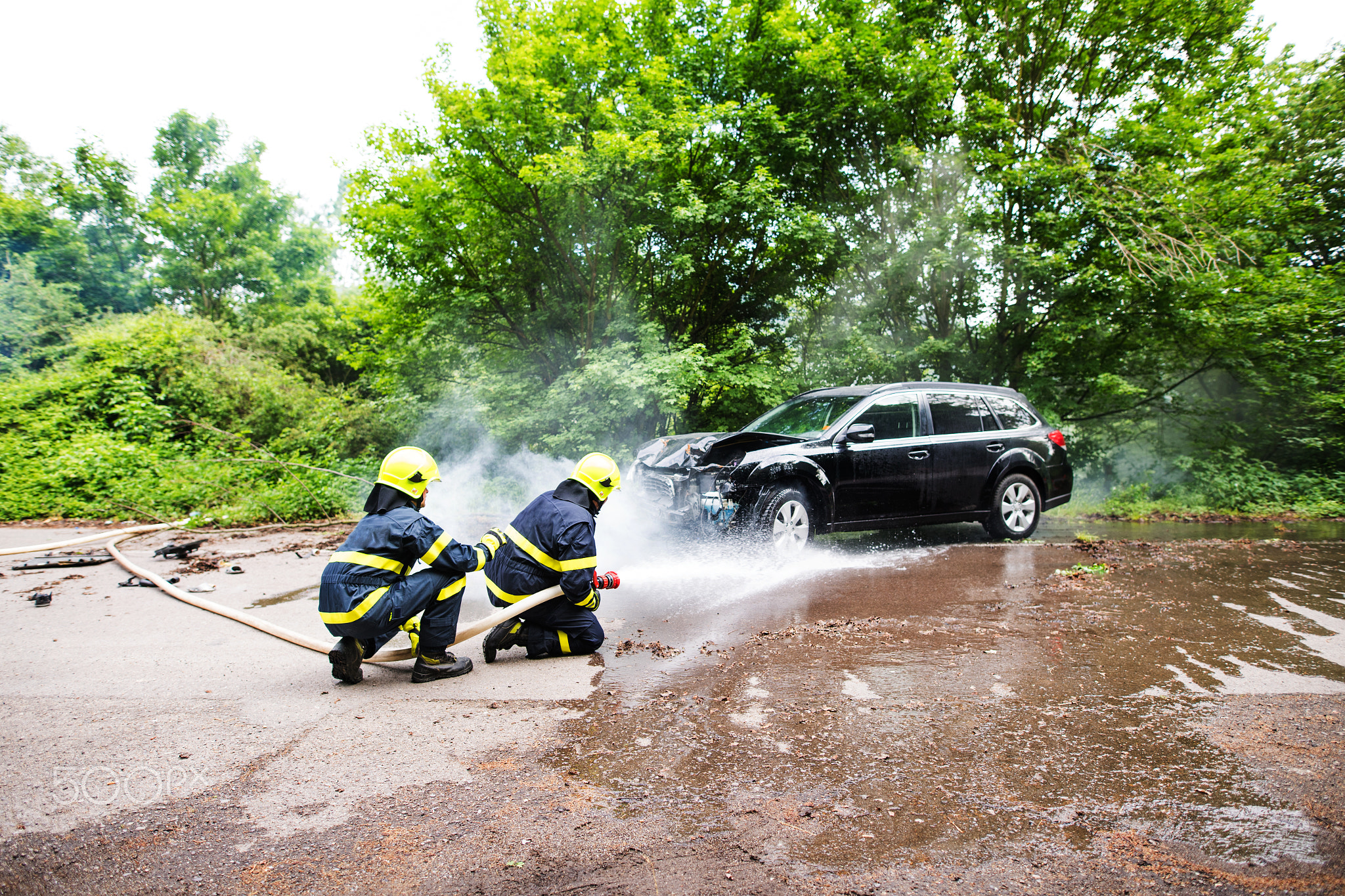 Two firefighters extinguishing a burning car after an accident.