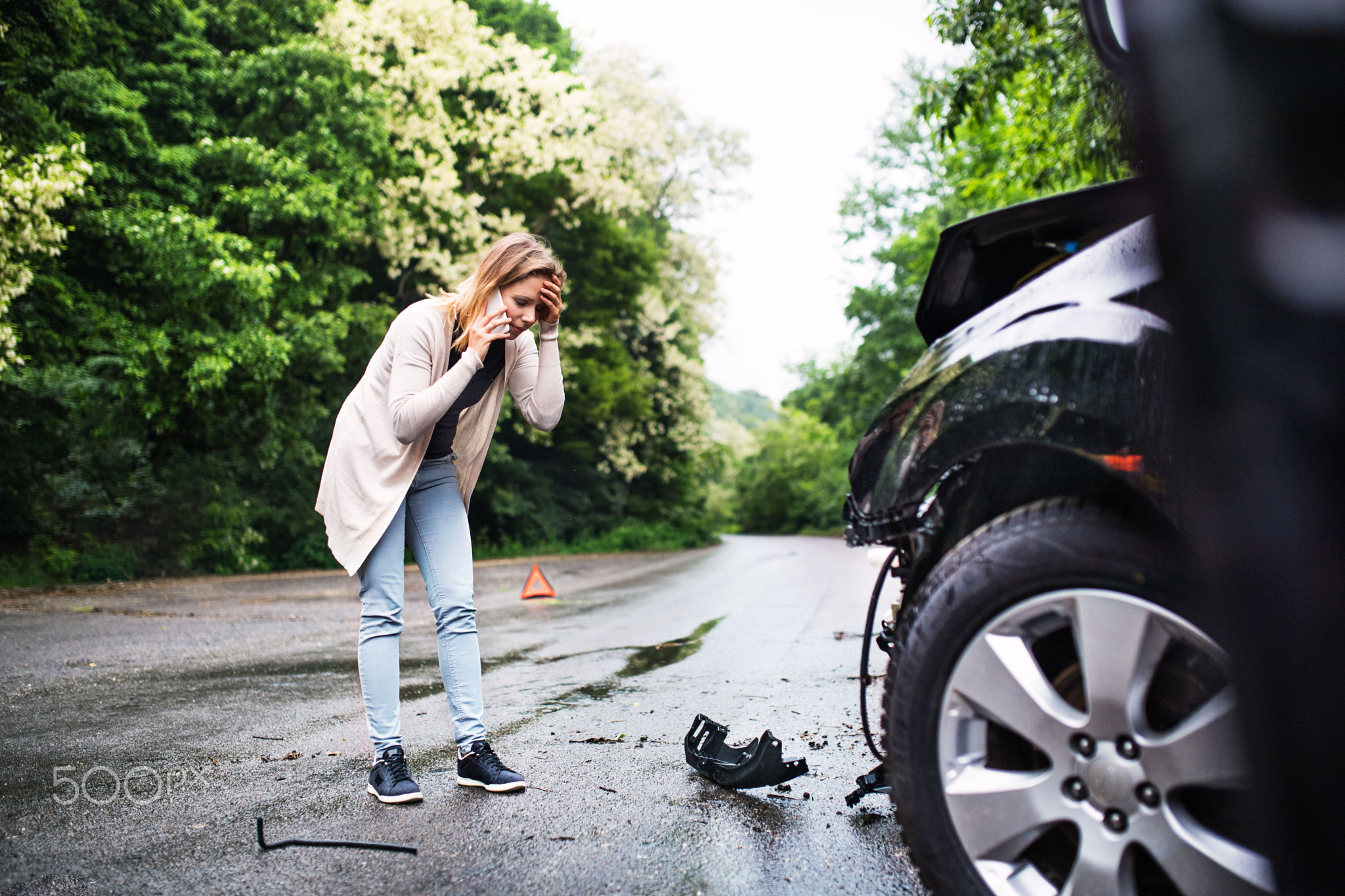 Young woman by the damaged car after a car accident, making a phone call.