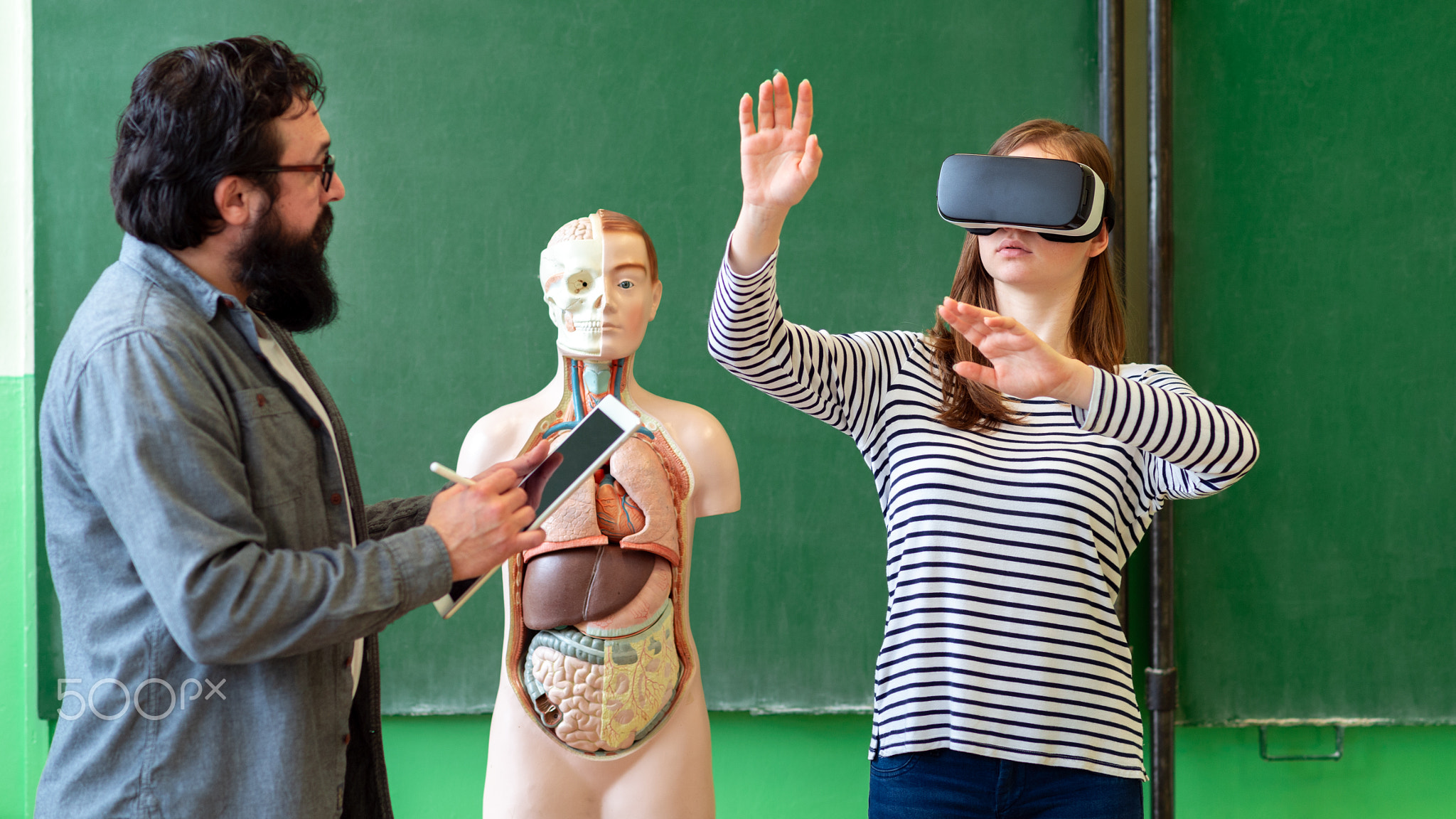 Young teacher using Virtual Reality Glasses and 3D presentation to teach students in biology...