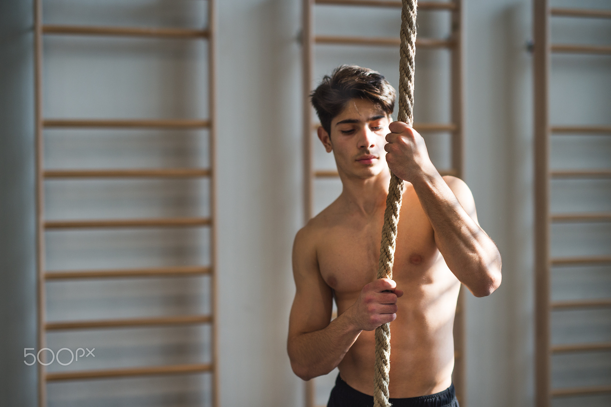 Fit young man in gym standing topless , holding climbing rope.
