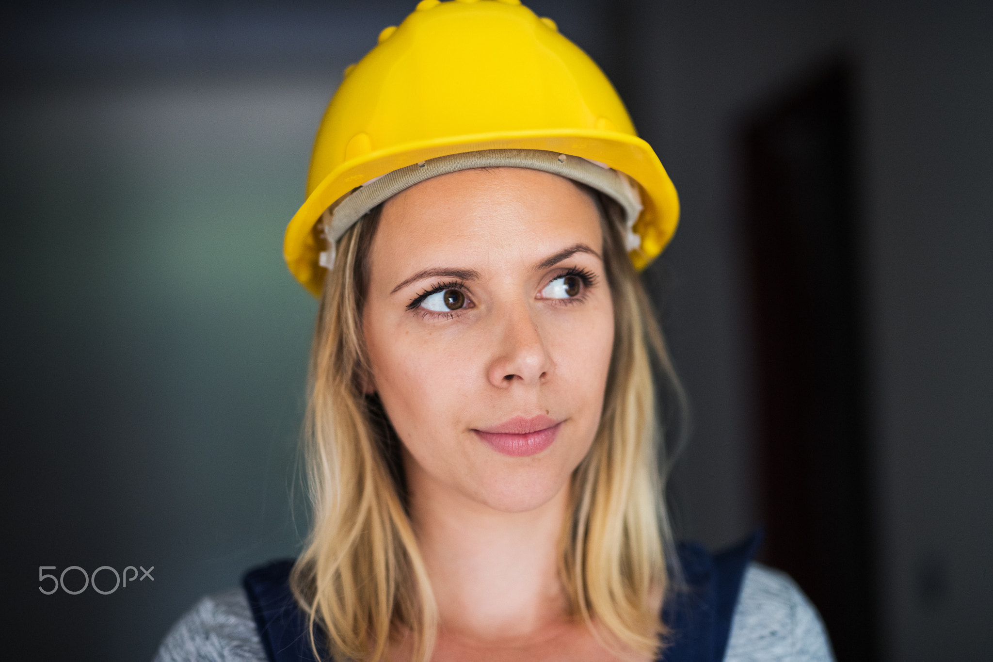 Young woman worker with a yellow helmet on the construction site.