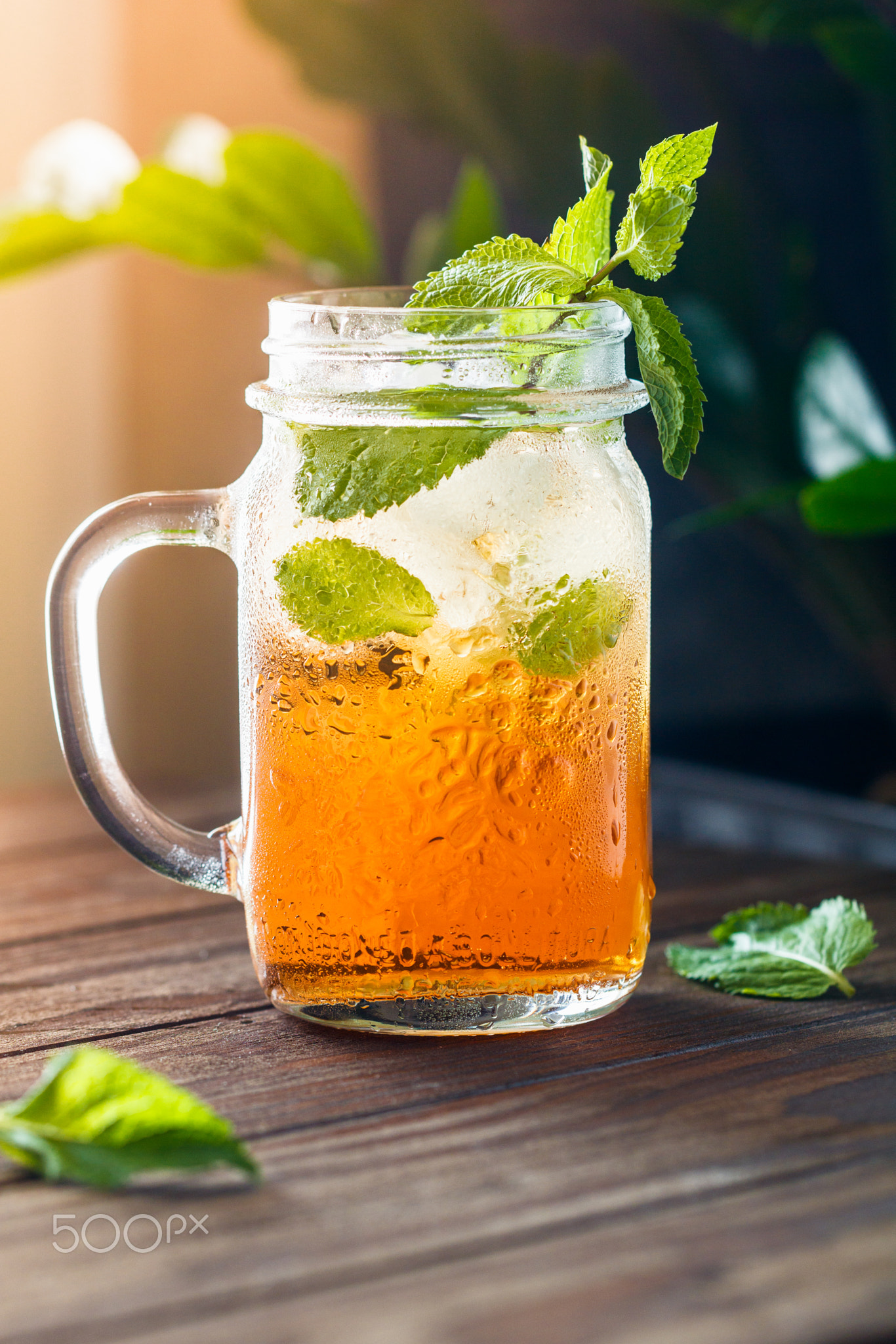 Ice black tea in a glass jar with fresh mint on a wooden table.