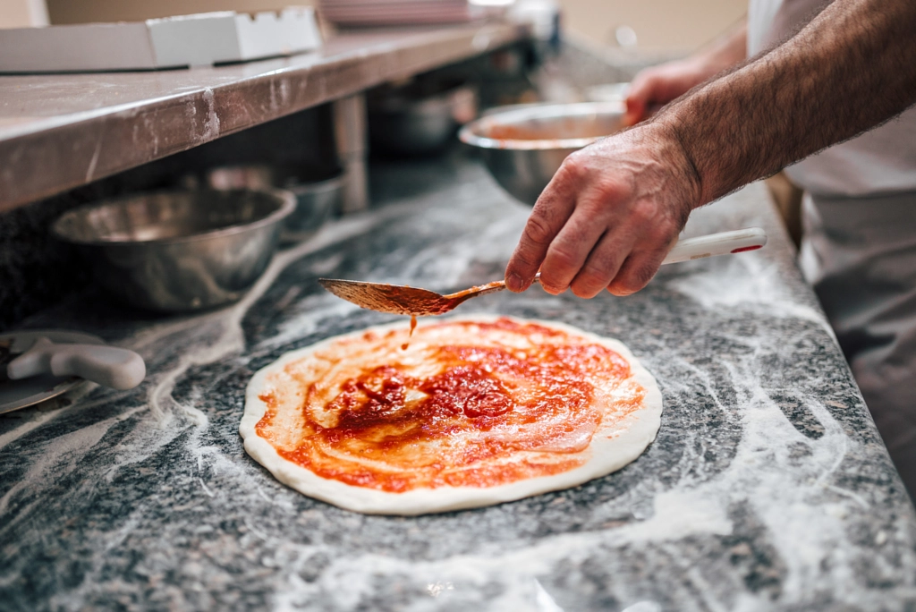 Preparing pizza. Chef's hand adding tomato sauce on pizza dough. by Branislav Nenin on 500px.com