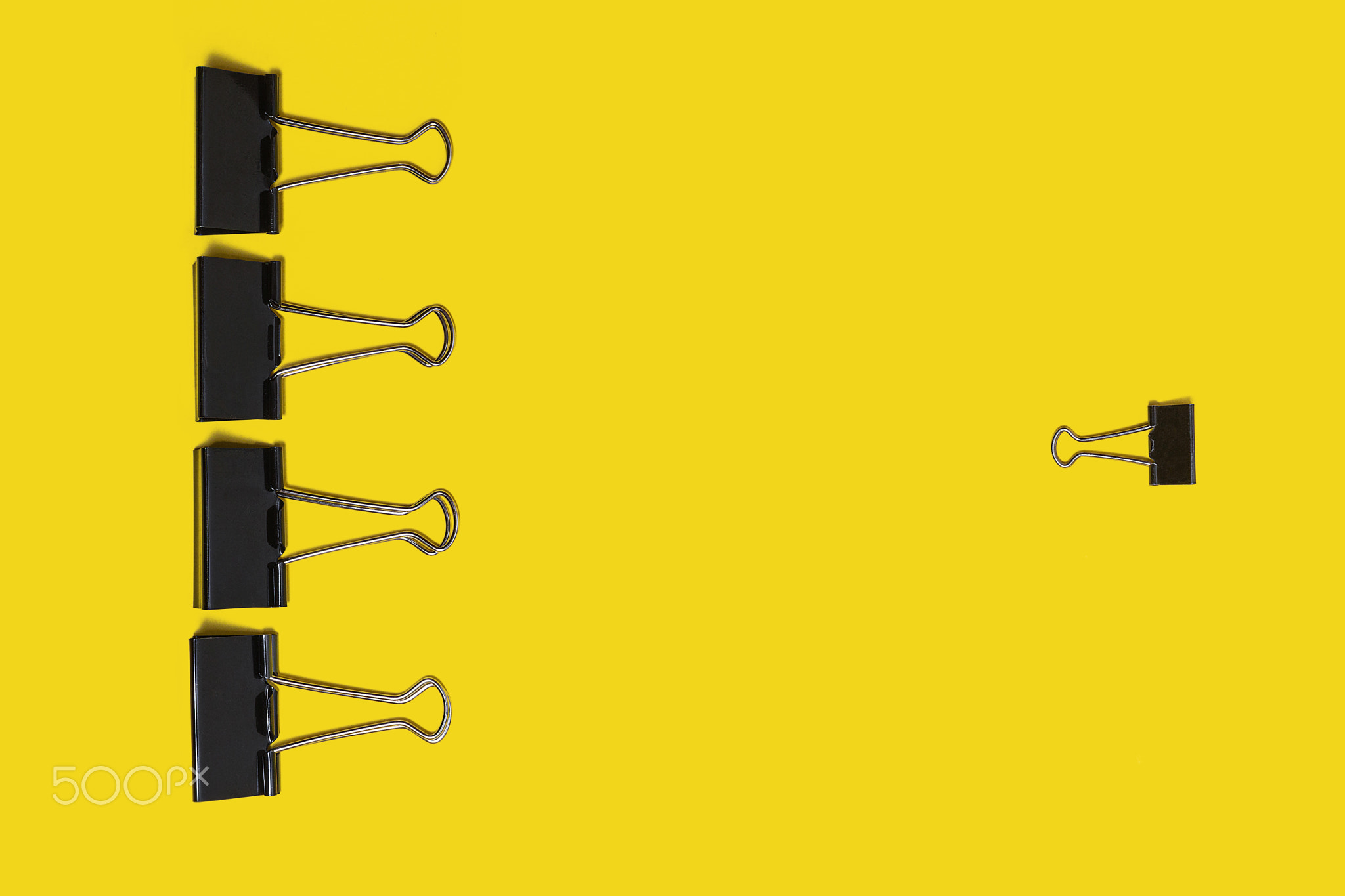 four big paper clips against small one lying on a yellow background