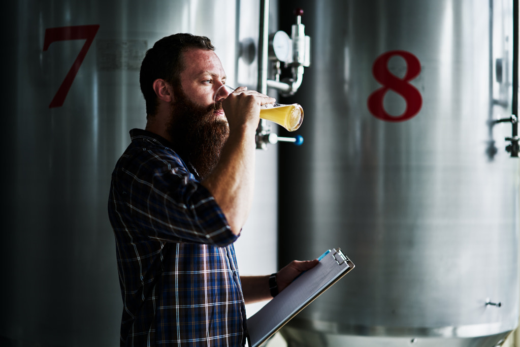 brewery worker conducting taste test of craft beer in front of fermenting tank by Joshua Resnick on 500px.com