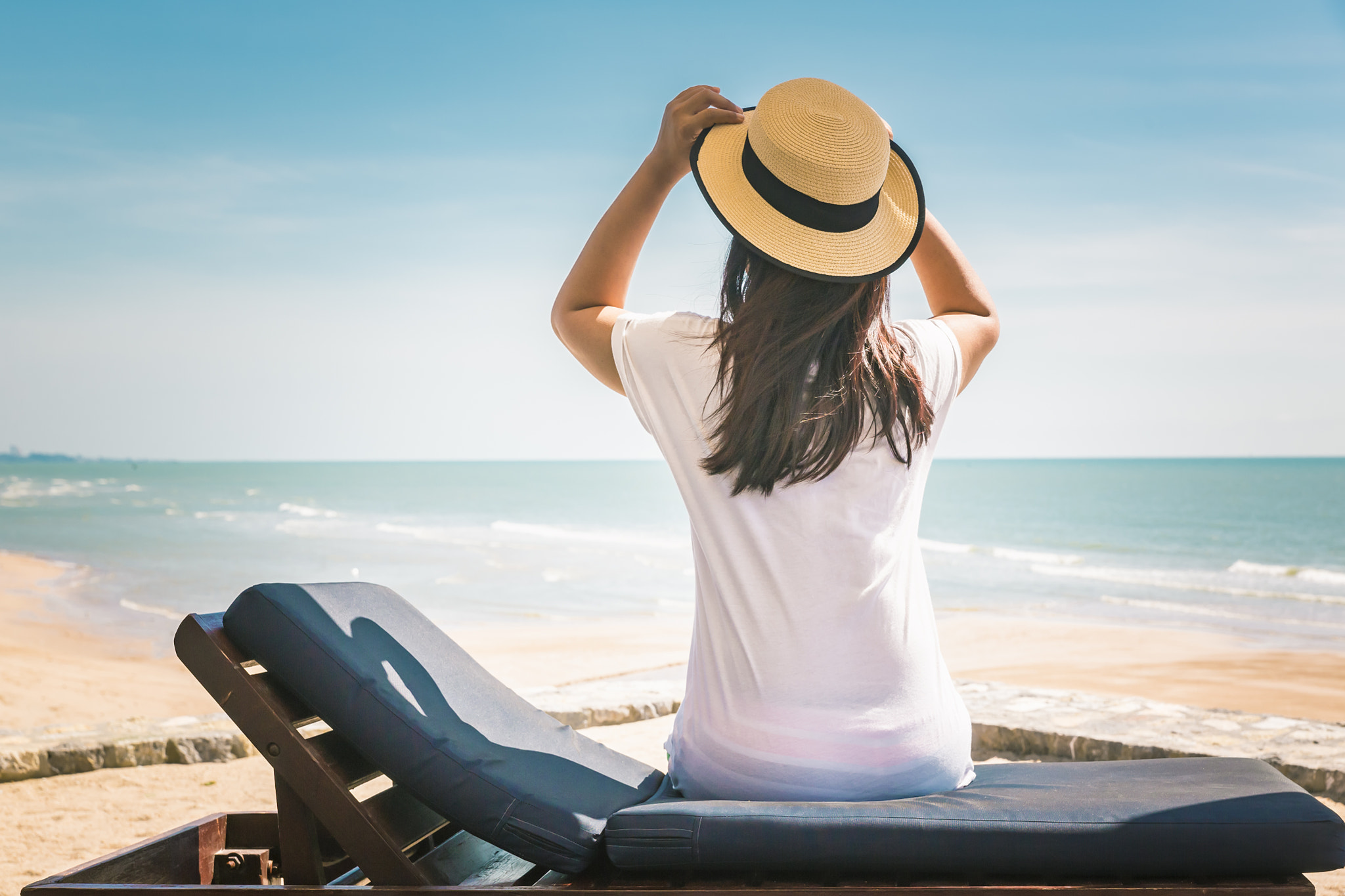 Woman relaxing on beach lounge chair or sun deck with sea view o