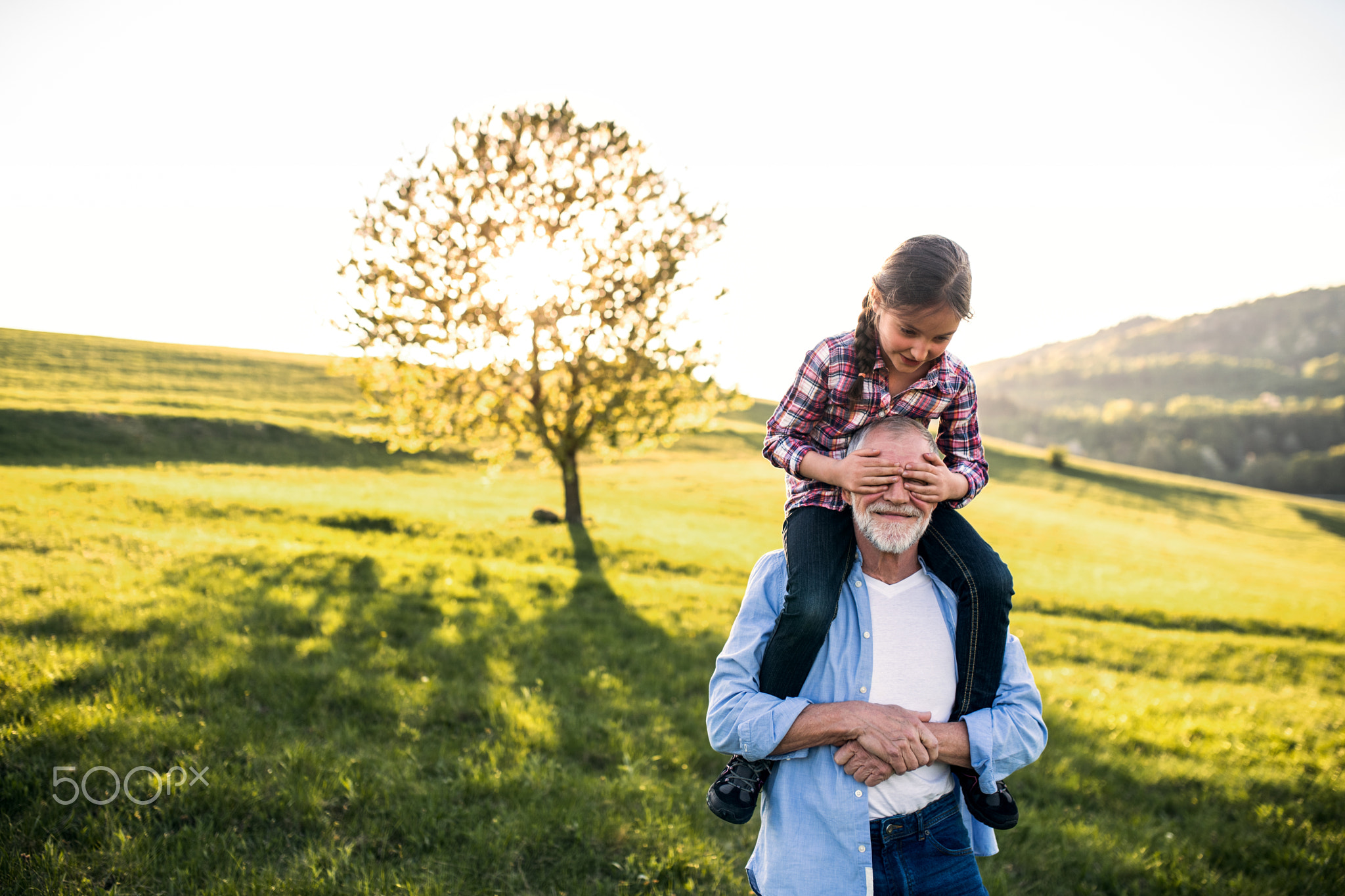 A senior grandfather giving a small granddaughter a piggyback ride in nature.