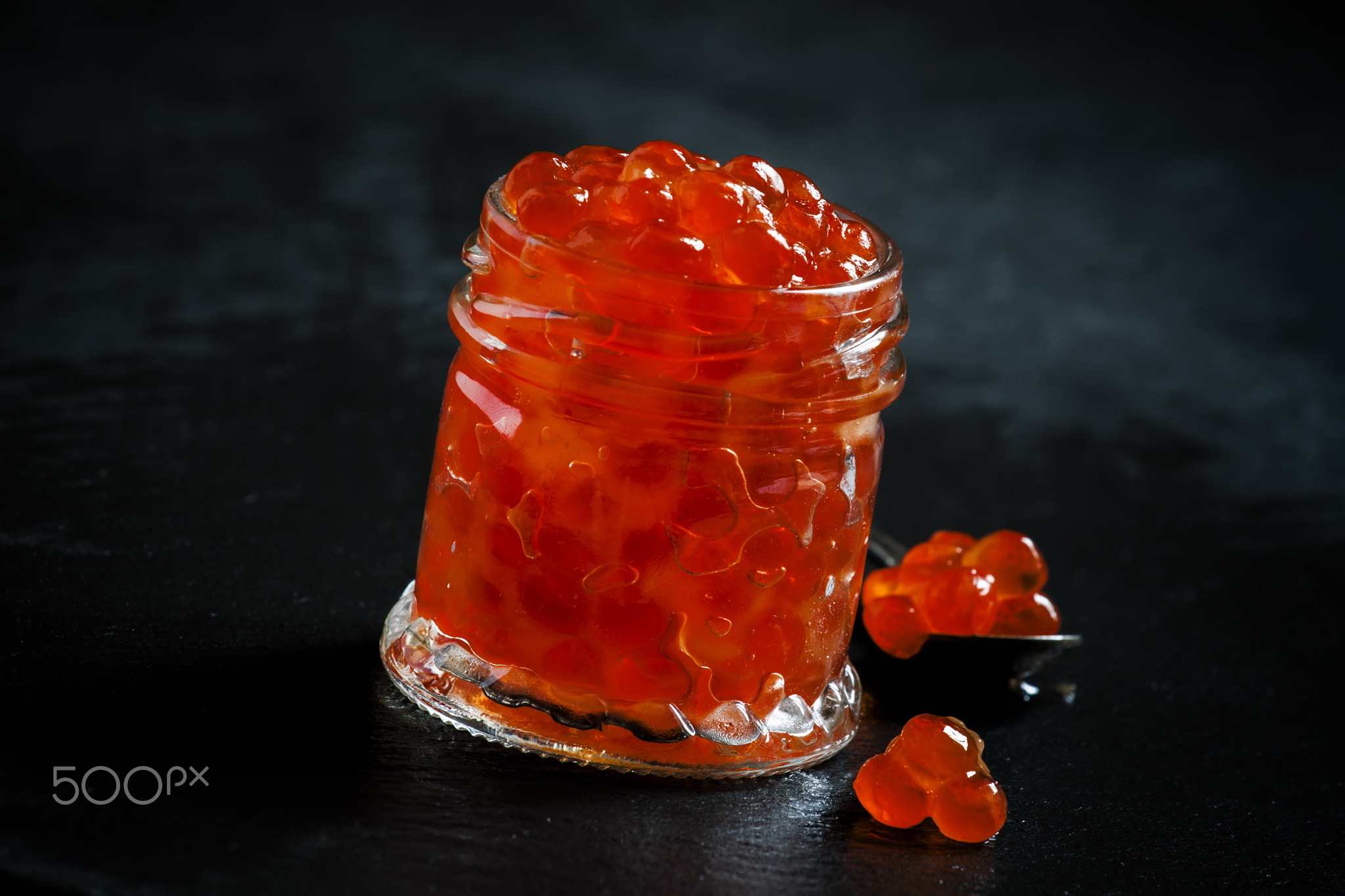 Red caviar in a glass jar on black stone background, selective f