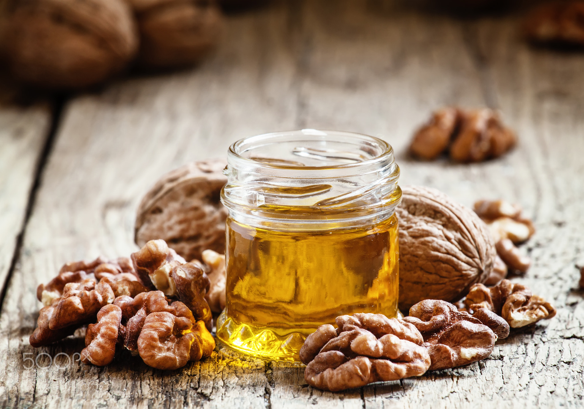 Walnut oil in a small jar and kernels on old wooden background i