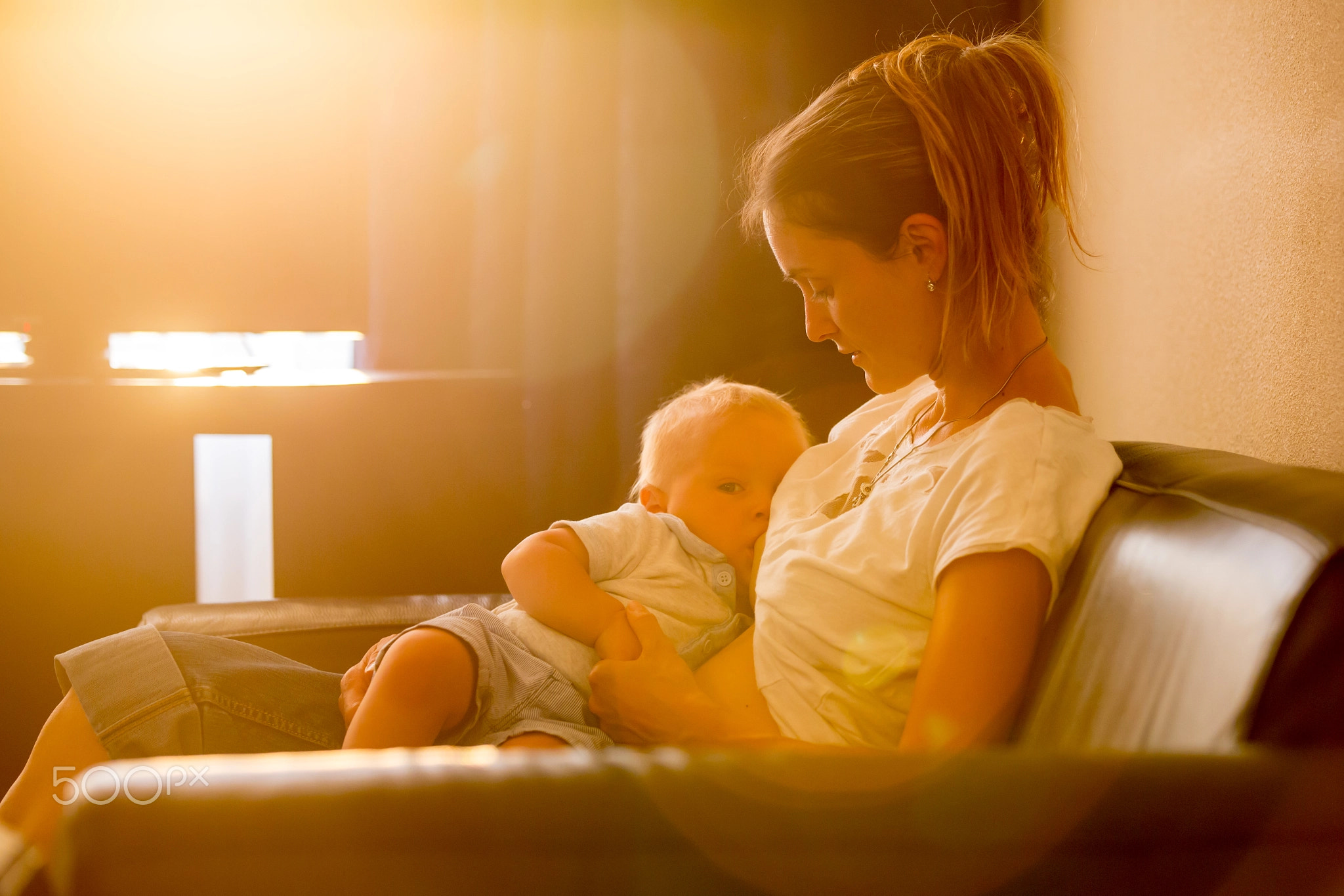 Young mother, breastfeeding on sunset on quiet evening her littl