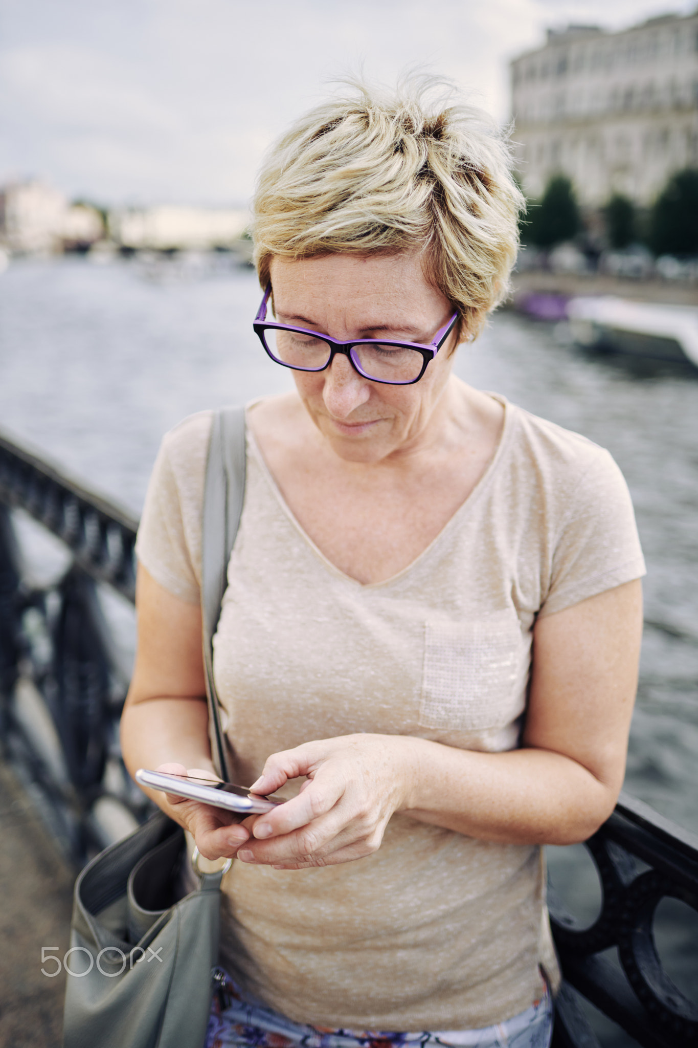 Aged woman browsing smartphone on embankment
