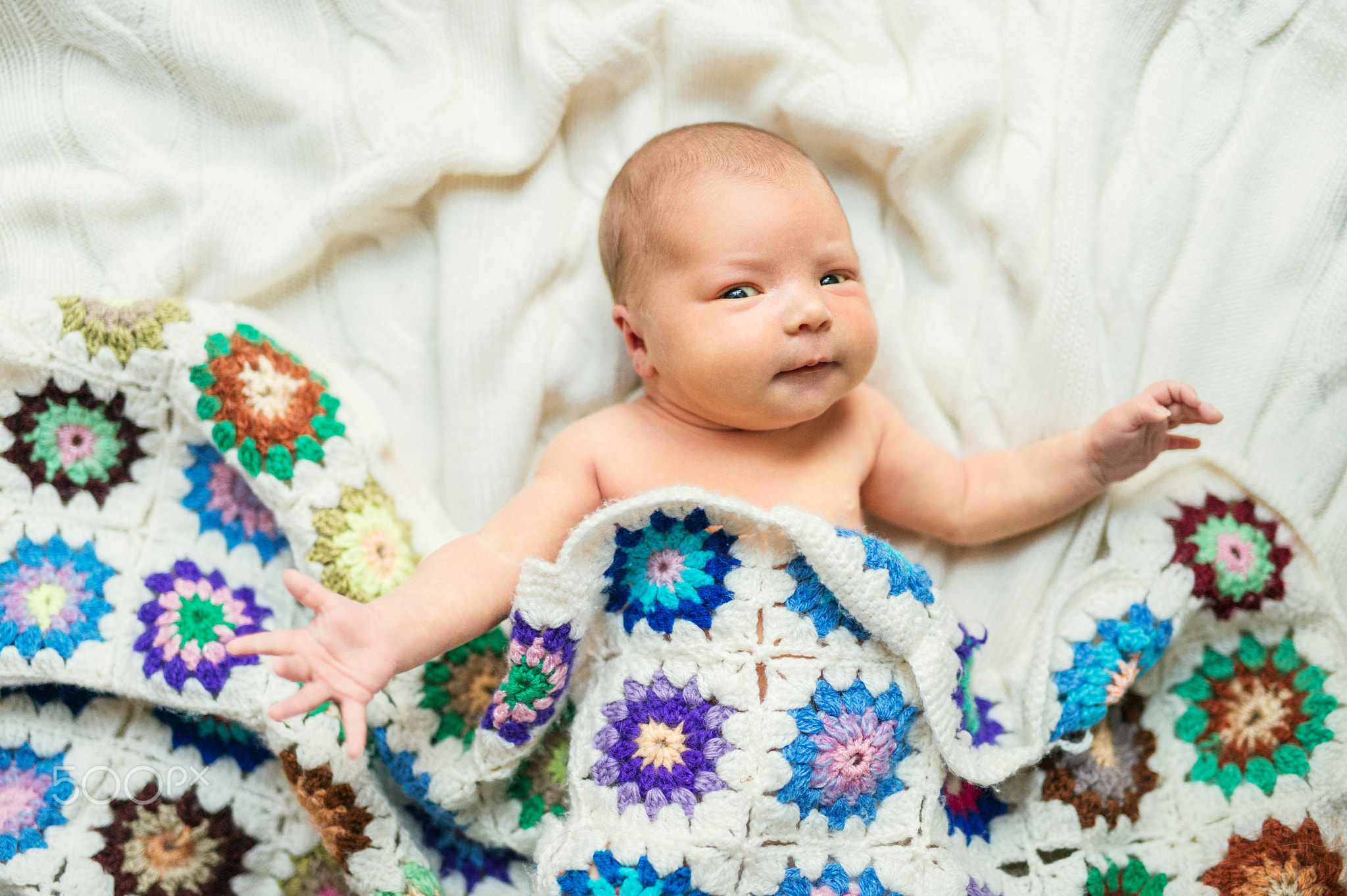 Newborn baby lying on bed, covered by a crocheted blanket. Top view.