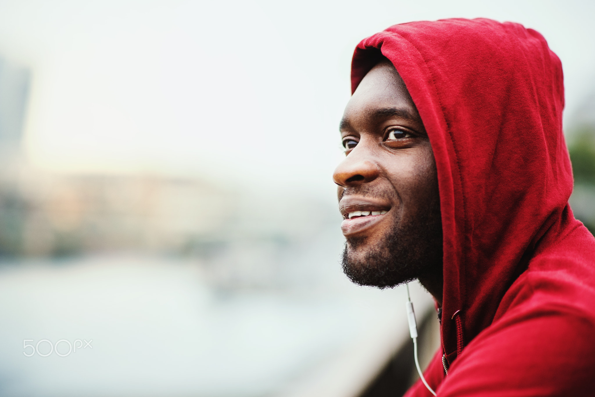 A close-up of black man runner with earphones and hood on his head in a city. Copy space.