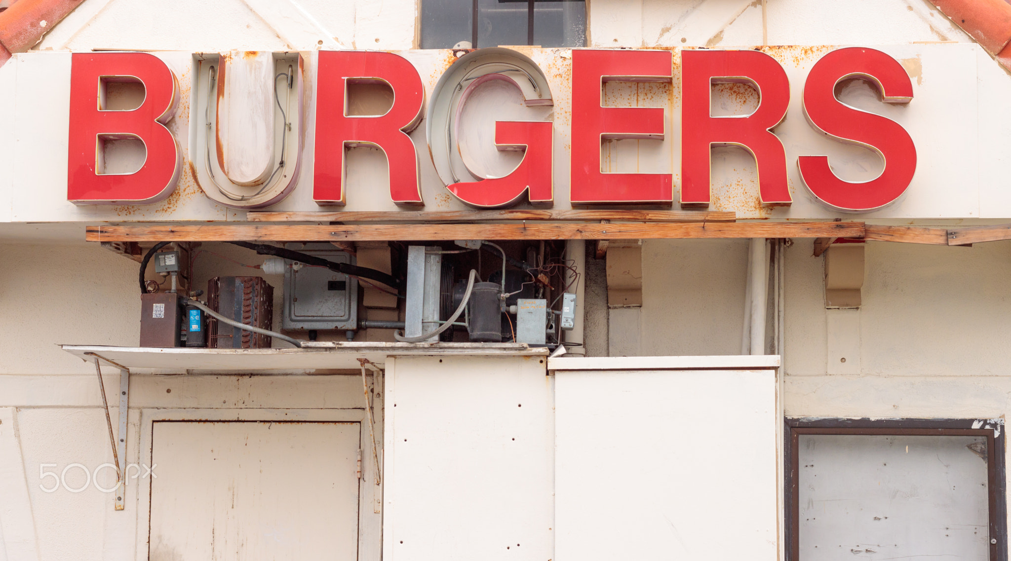 Retro red burger sign from the 60s in disrepair, rusty gray electrical boxes and conduit below...