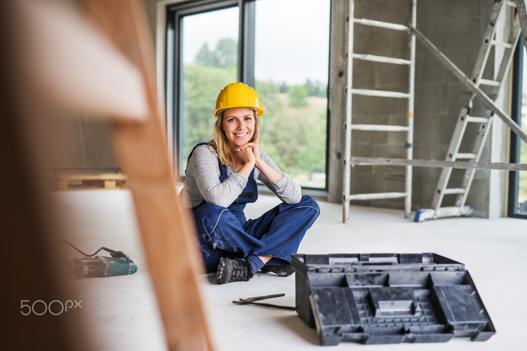 Young woman worker sitting on the floor on the construction site.