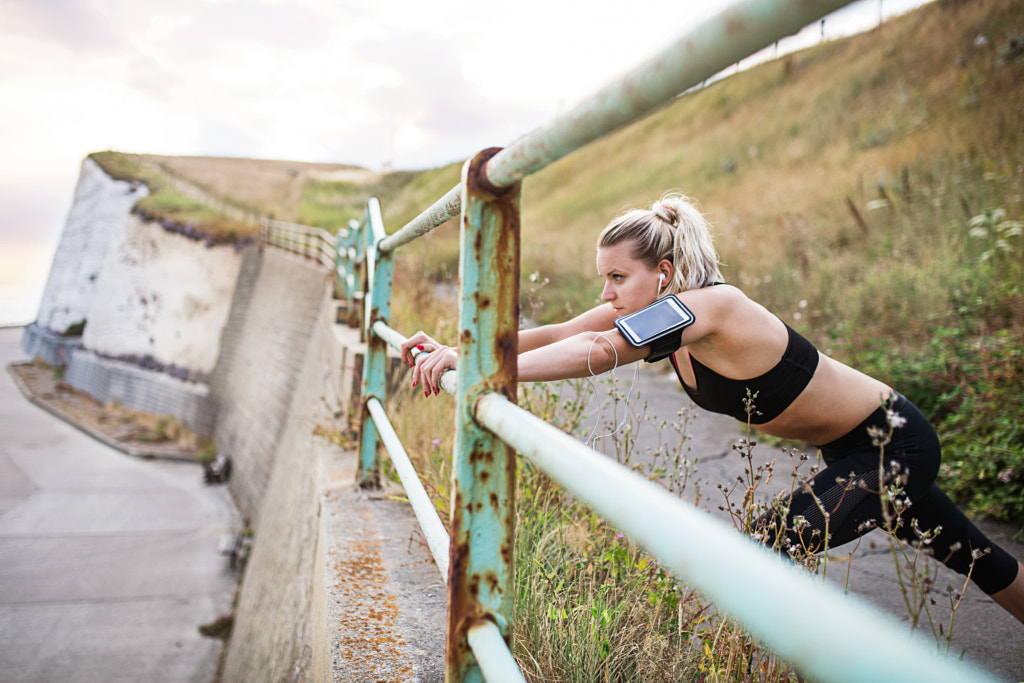 Young sporty woman runner with smartphone stretching on the beach outside. by Jozef Polc on 500px.com