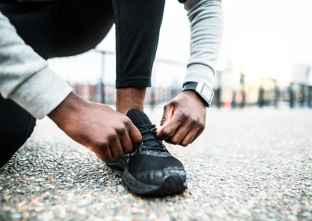 A close-up of a young sporty black man runner tying shoelaces outside in a city. by Jozef Polc on 500px.com