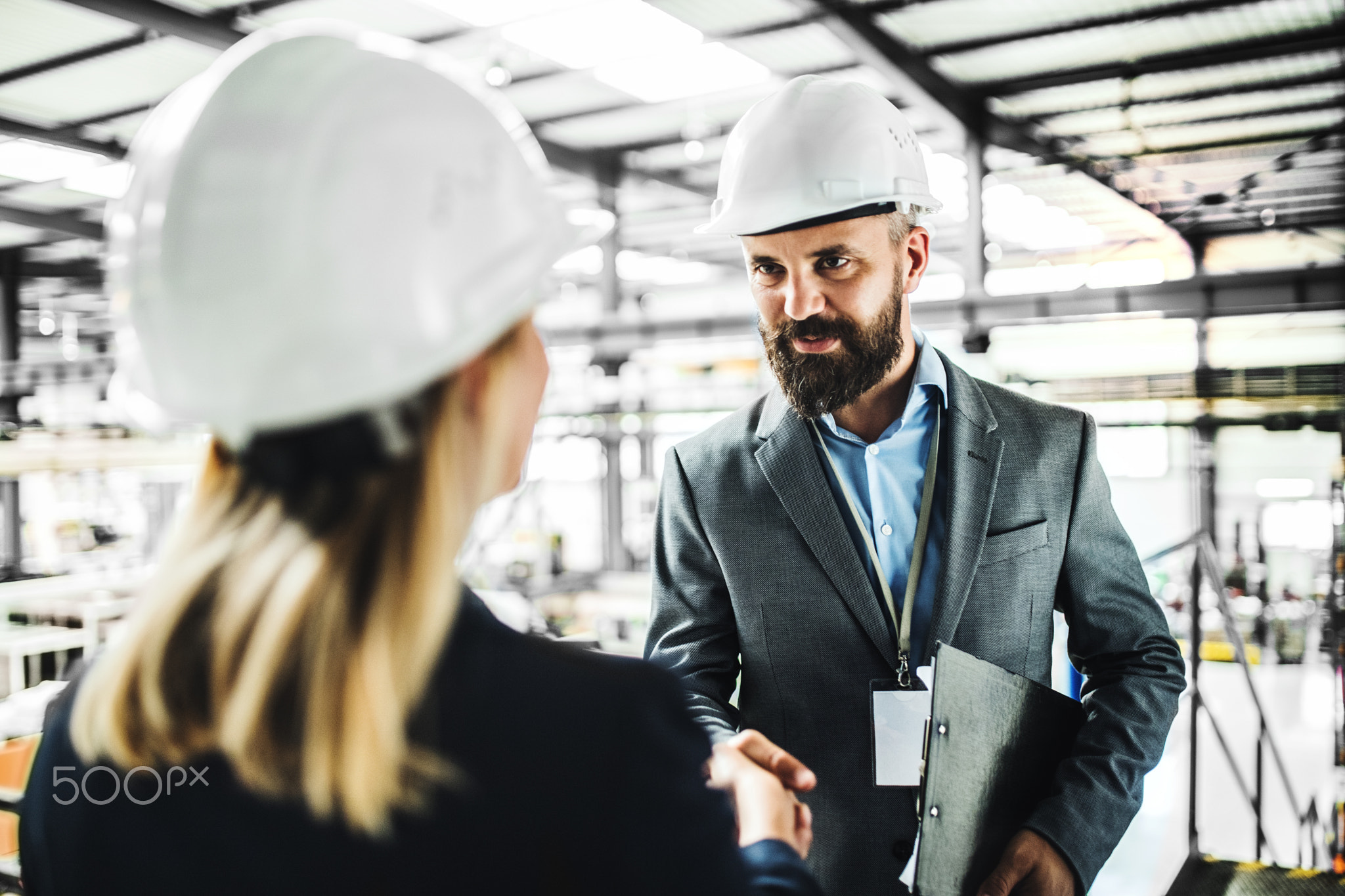 A portrait of an industrial man and woman engineer in a factory, shaking hands.