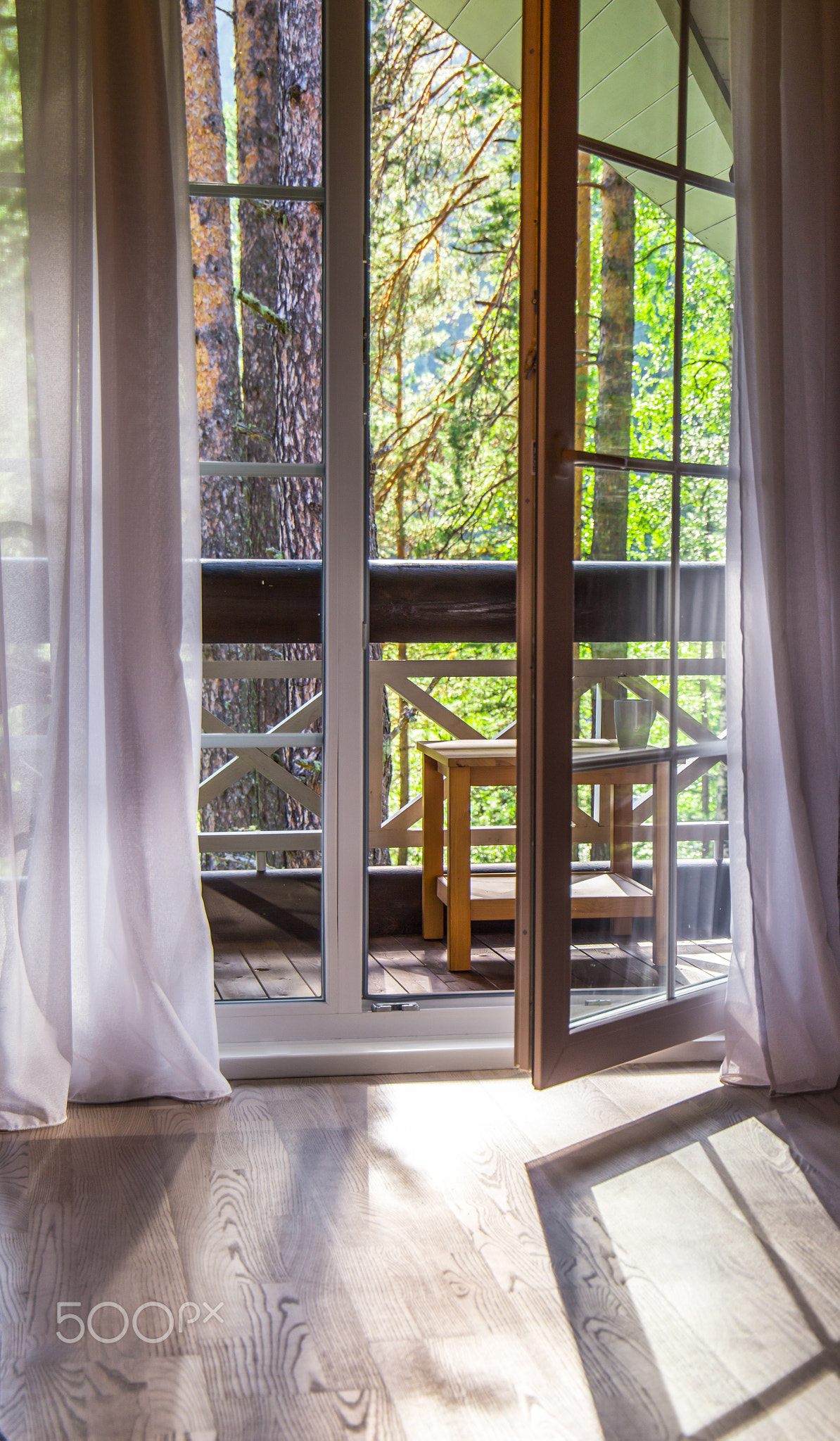 French doors open onto a balcony with a view of leafy green trees. nature. relax concept. vocations