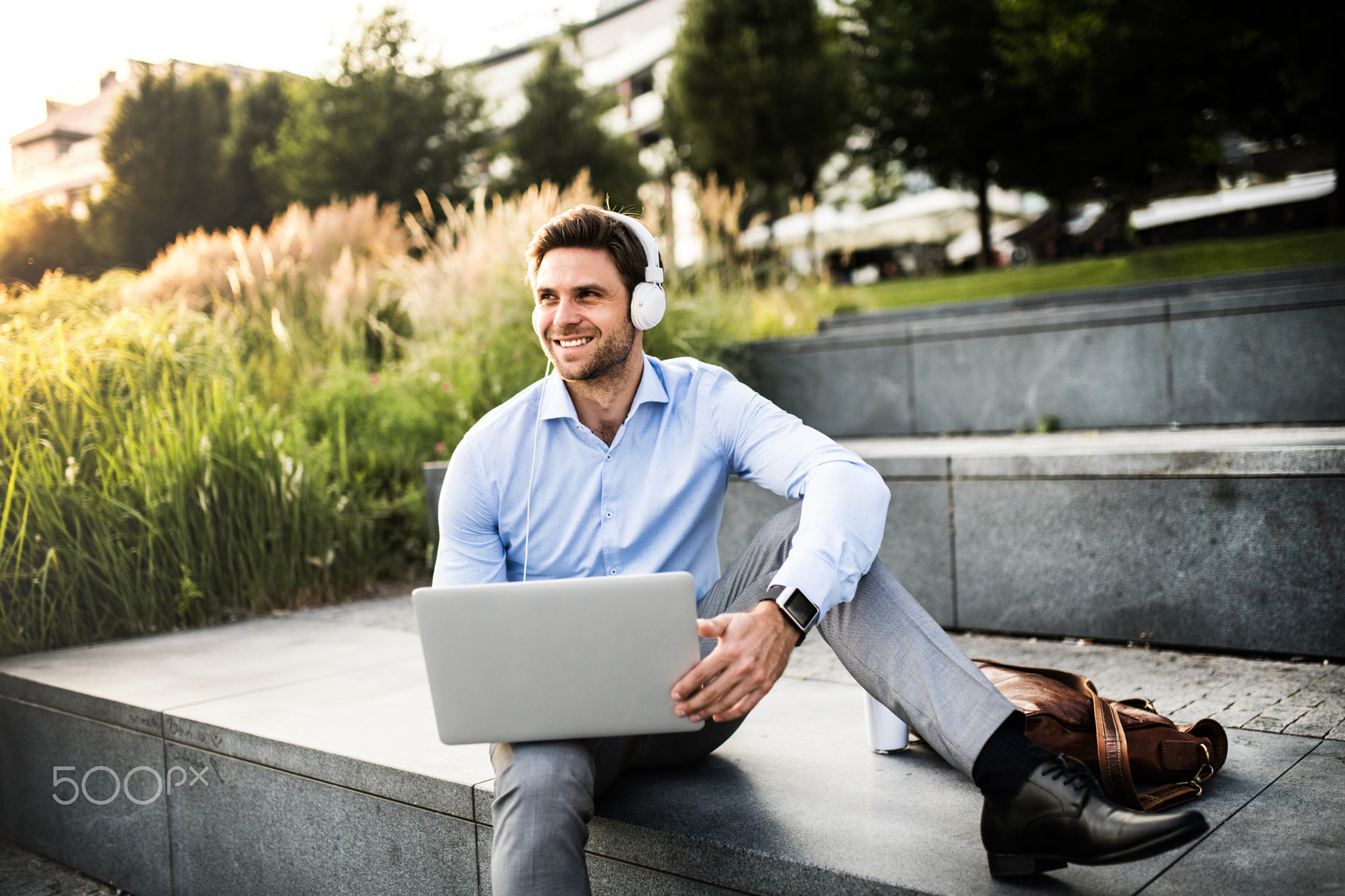 A businessman with headphones sitting outdoors on stairs, listening to music.