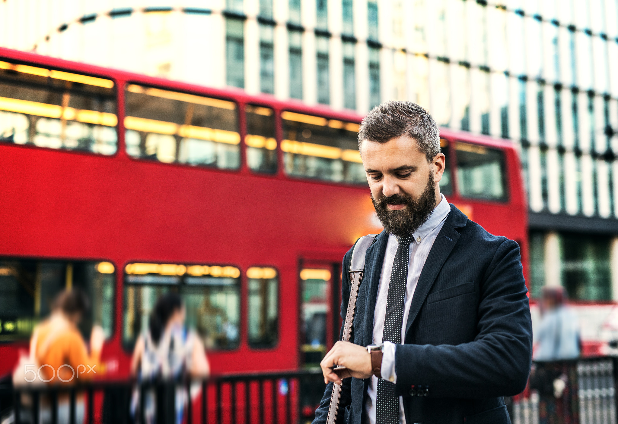 Hipster businessman waiting for the bus in London, checking the time.
