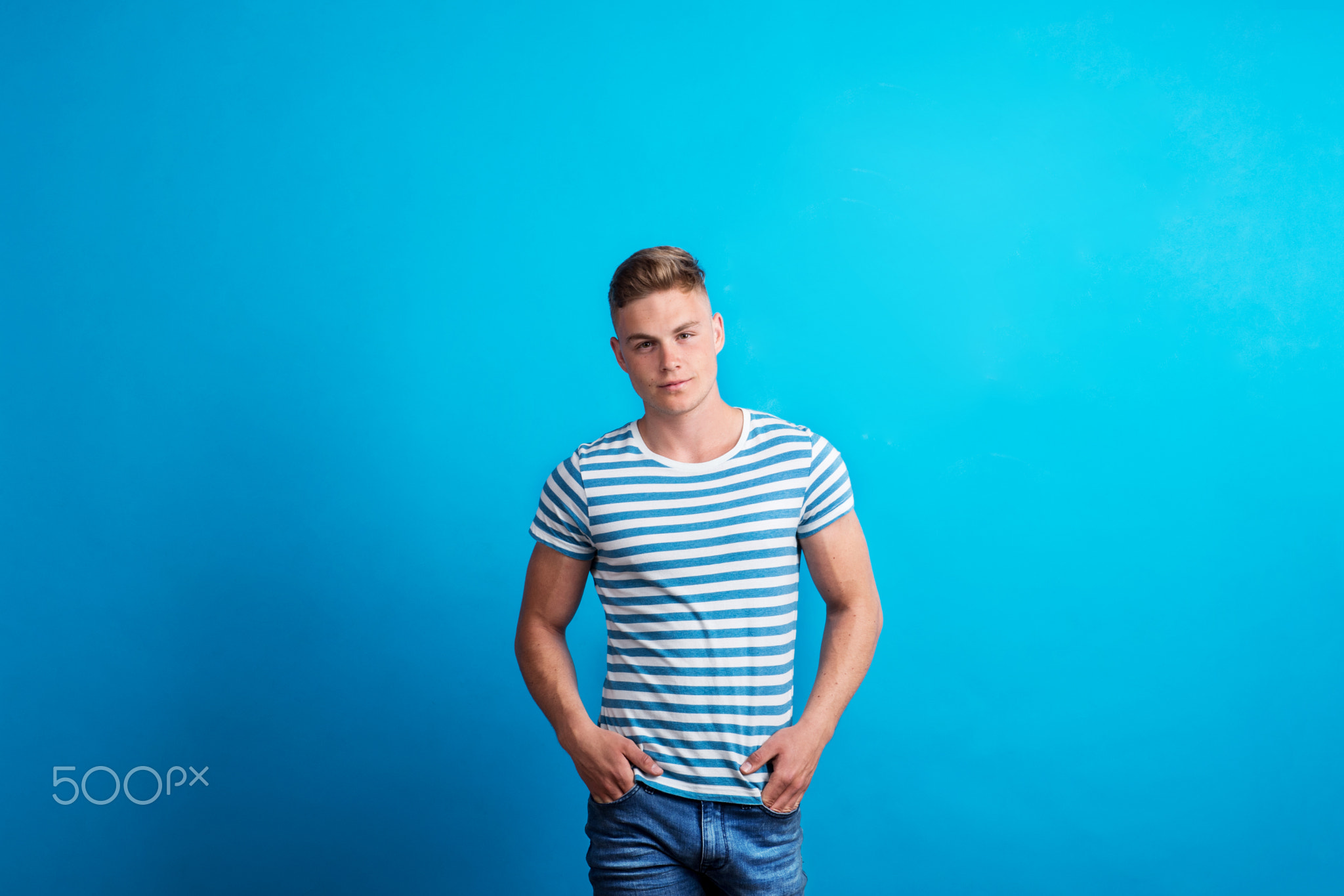 Portrait of a young man in a studio standing against blue background.
