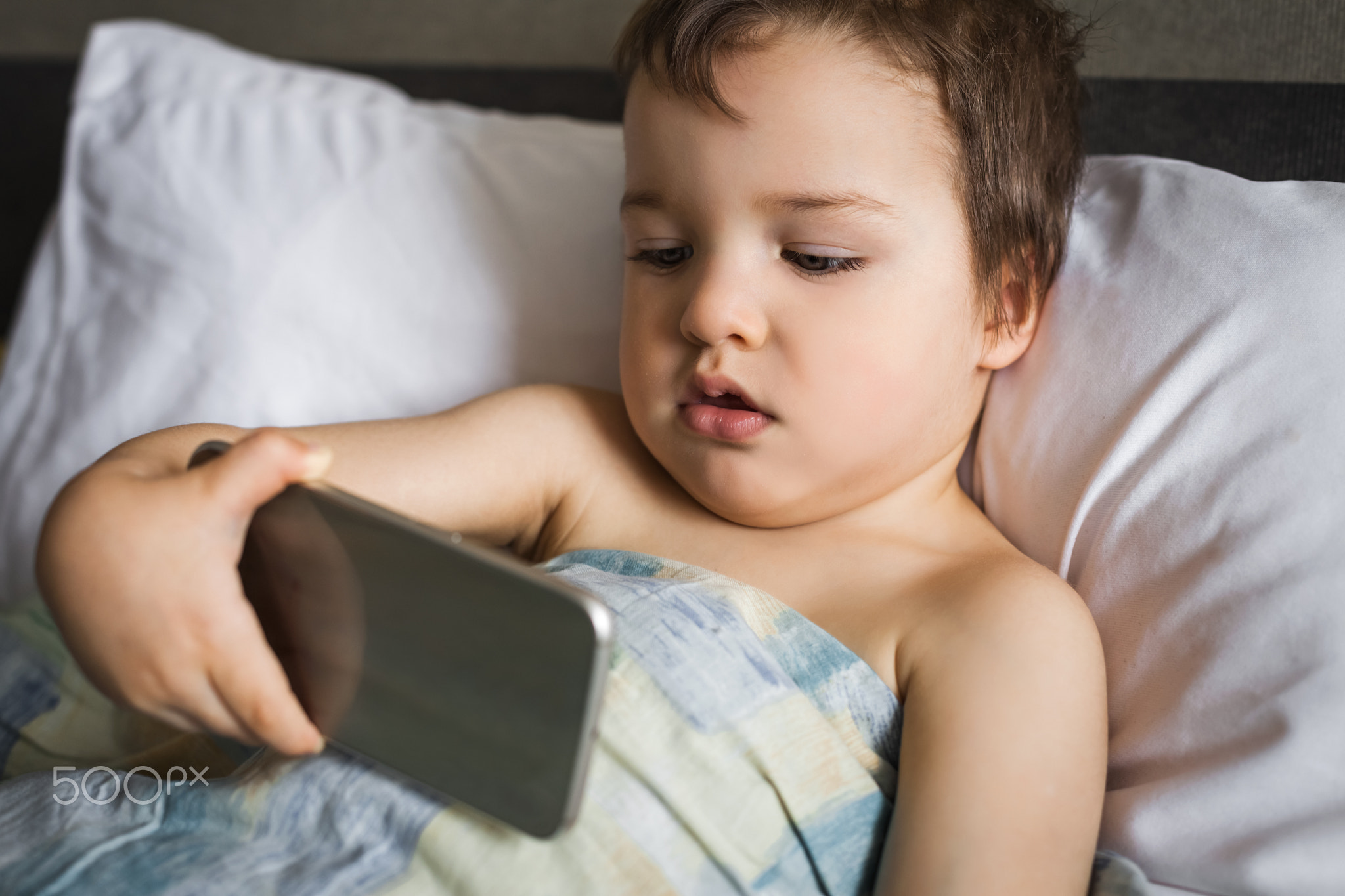 smart cute boy holding phone lying on the bed in morning