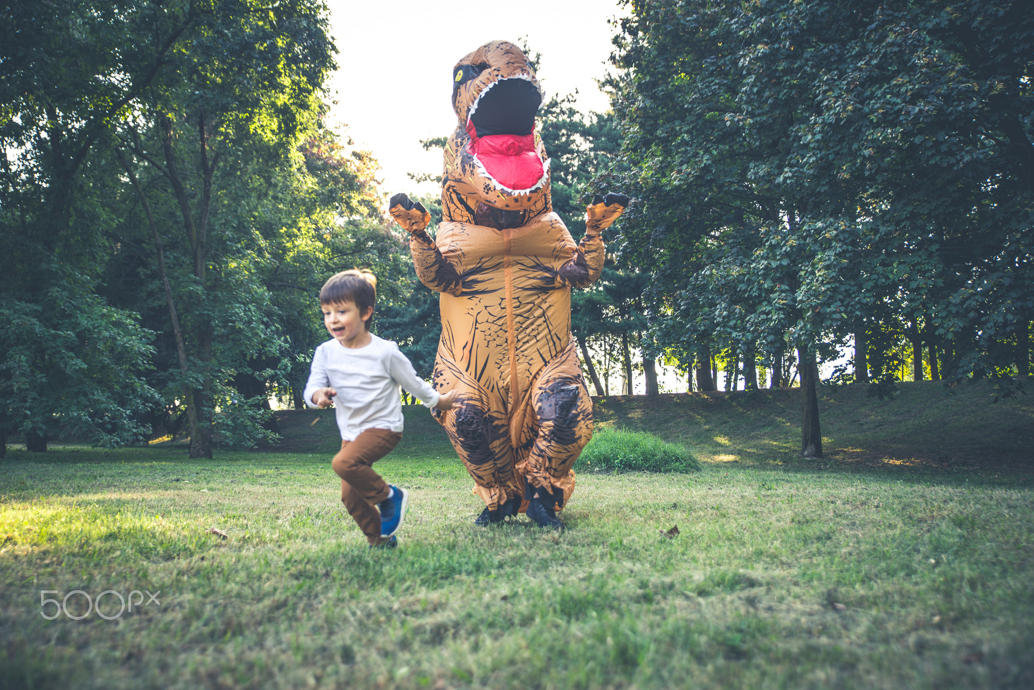 Father and son playing at the park, with a dinosaur costume, hav