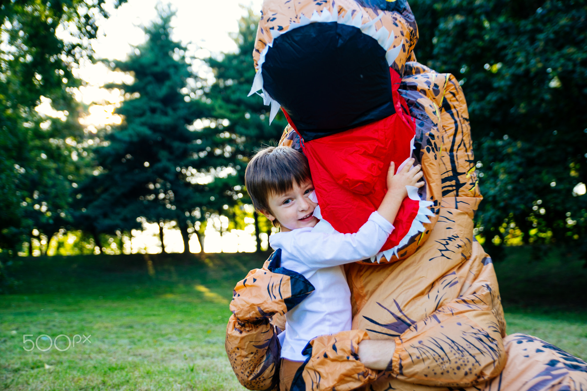 Father and son playing at the park, with a dinosaur costume, hav