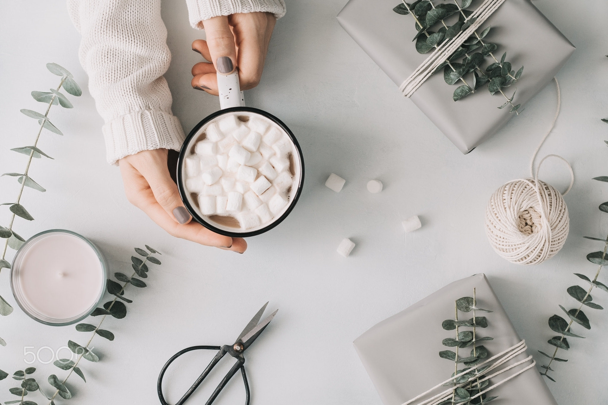 Girl's hands hold a mug with hot chocolate and marshmallow among gift boxes and eucalyptus on a...