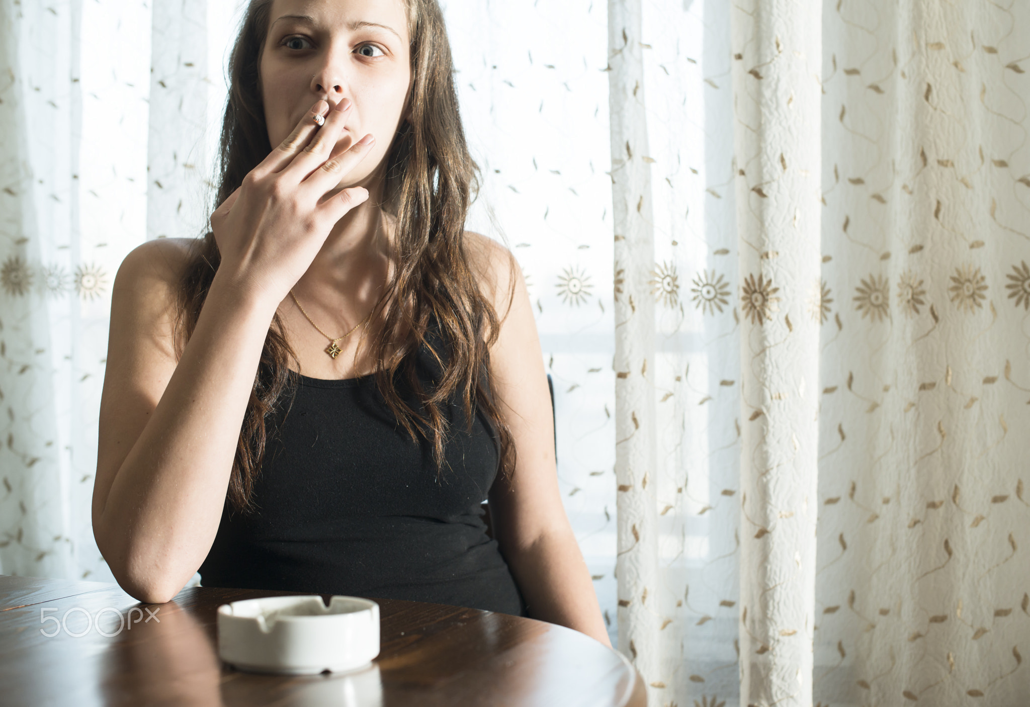 Girl smokes cigarette and holds ashtray.