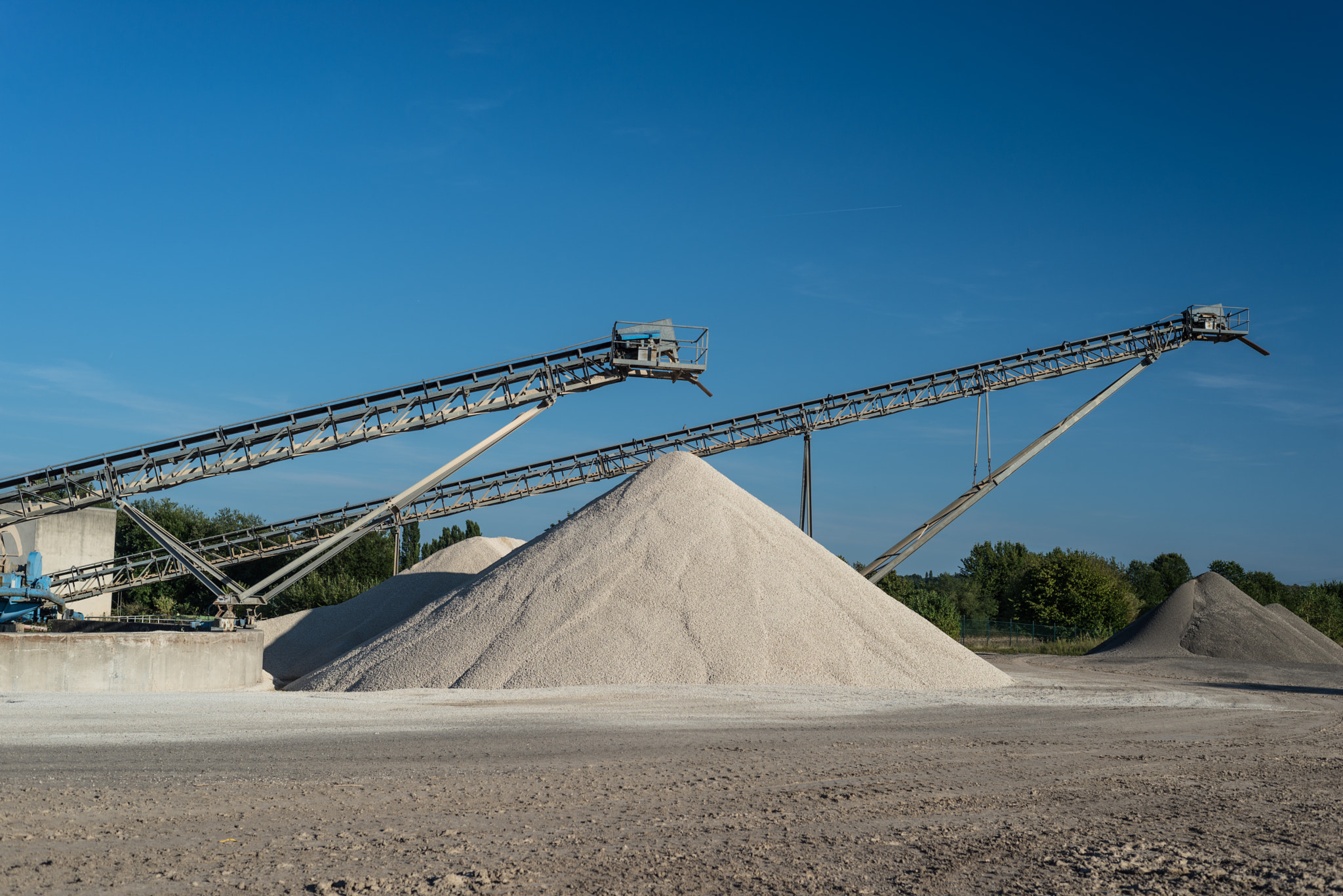 Conveyor over heaps of gravel on blue sky at an in