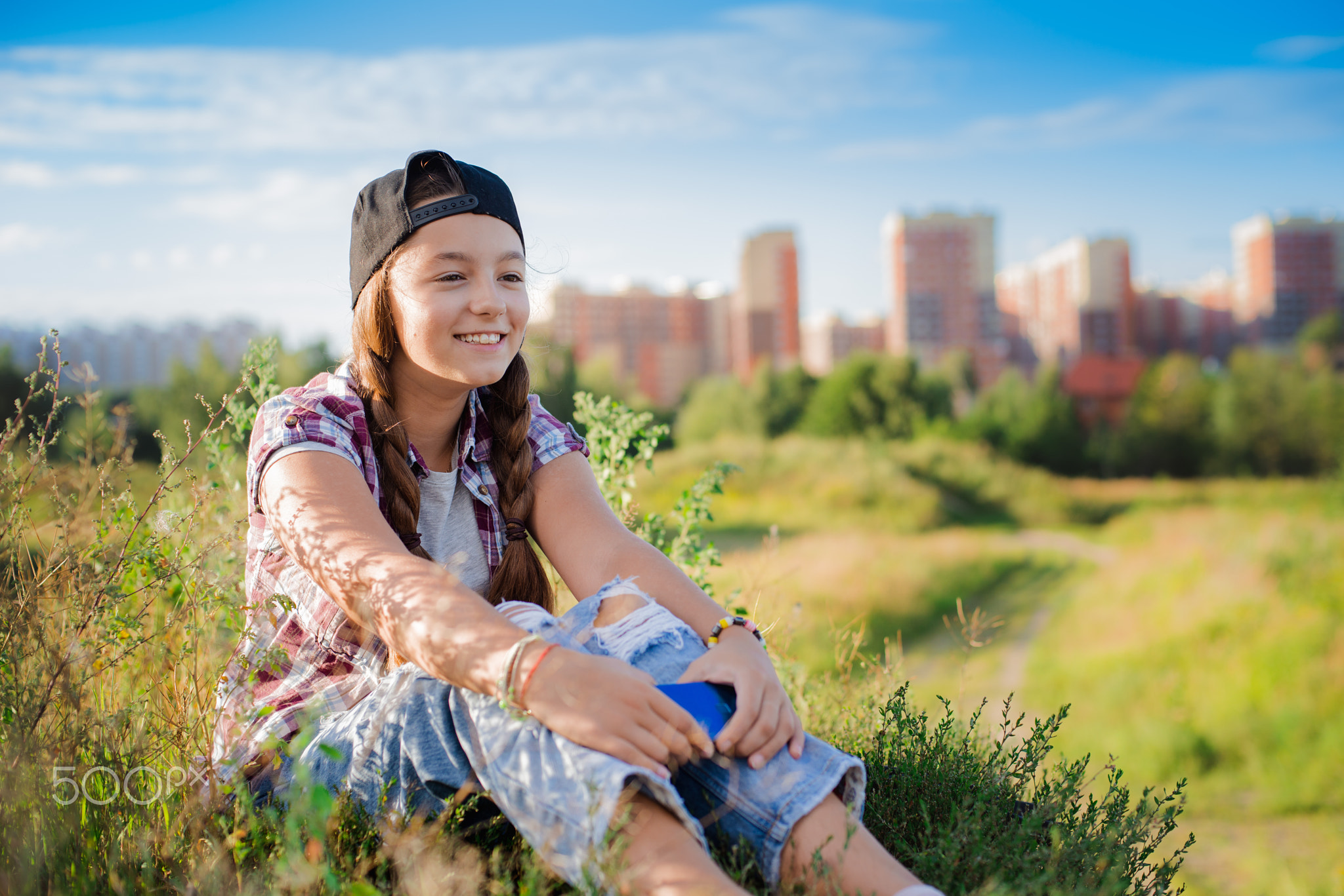 girl teenager in glasses sits the ground city background in the headphones of selfie smartphone